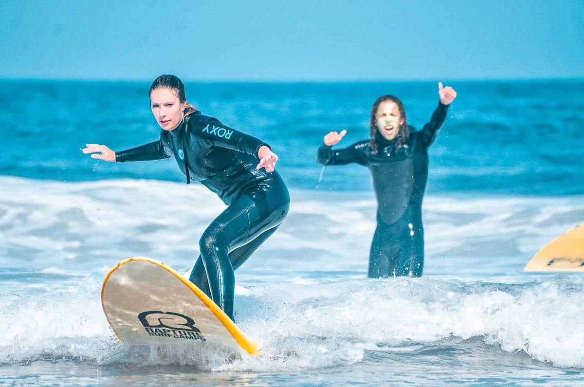 A girl surfing while another person cheers her from behind.