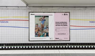 Kunstplakatierung am U-Bahnhof Feldstraße. Das Plakat zeigt das Kunstwerk "Would be nice" von Stephan Hohenthanner: Zwei Männer liegen auf Liegen in der Sonne. Hinter Ihnen geht eine Frau, die sich ihren Badeanzug auszieht.