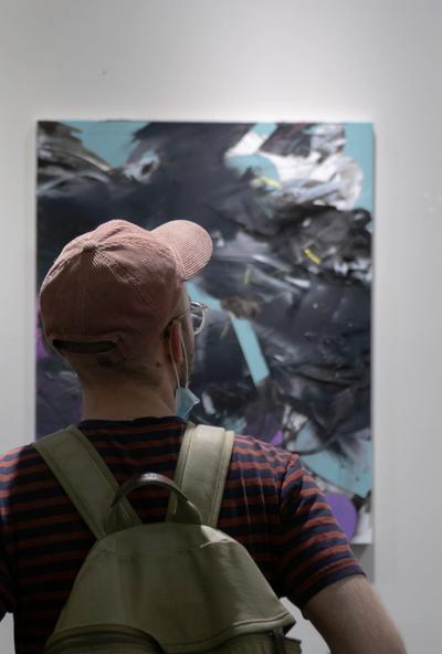 Ein Mann mit pinker Kappe und Rucksack von hinten vor einem Kunstwerk.