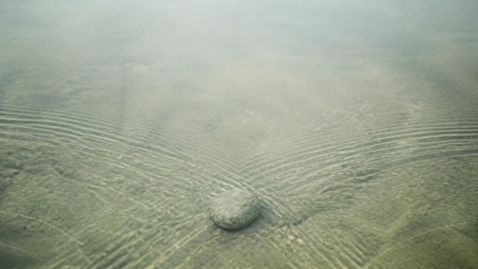 A figure rests at the threshold of water and reflected light.