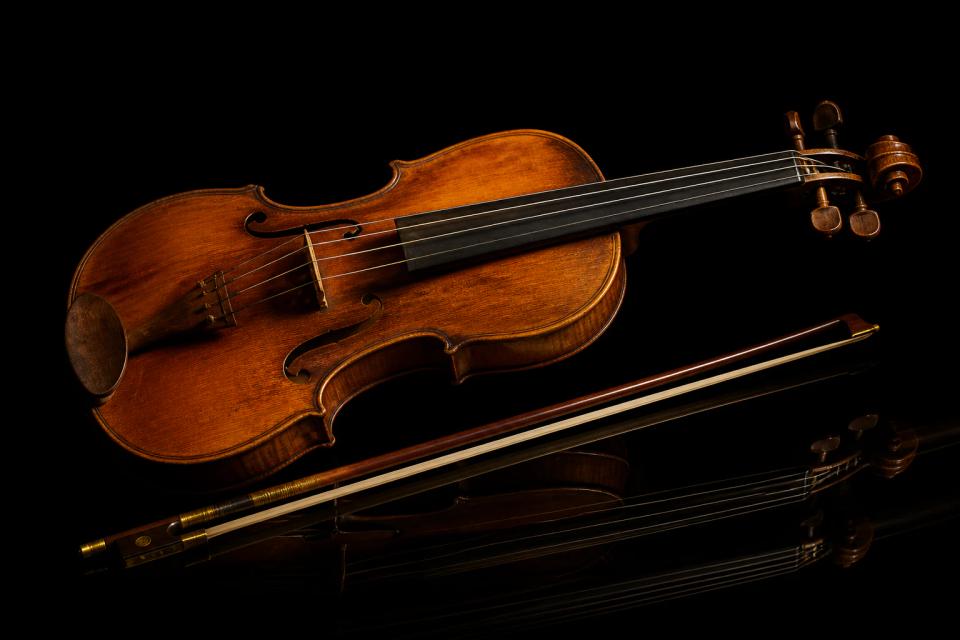 A Baroque violin and bow on a glossy black surface.