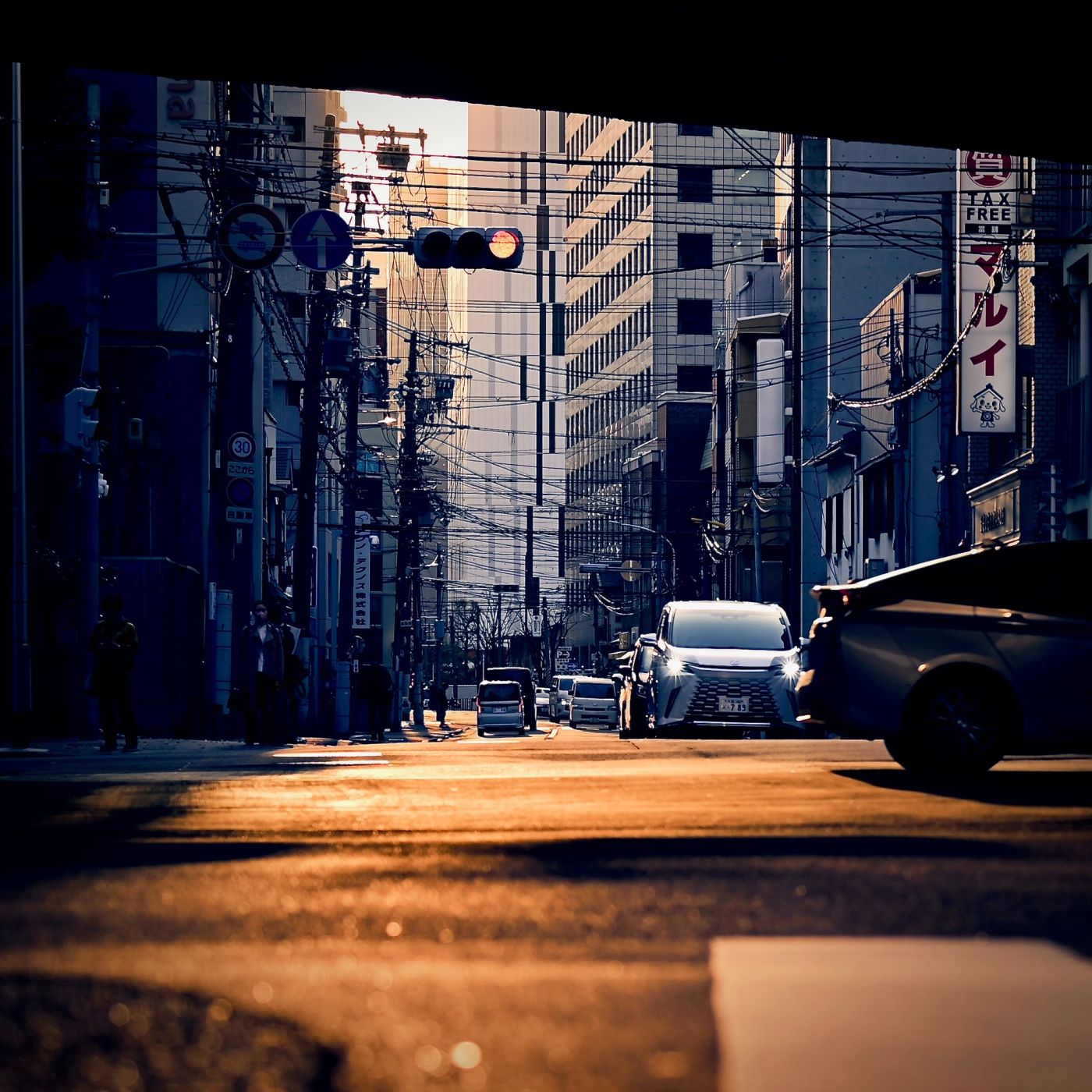 View of the street in Osaka during the golden hour with passing by vehicles, stoplights, hanging powerlines