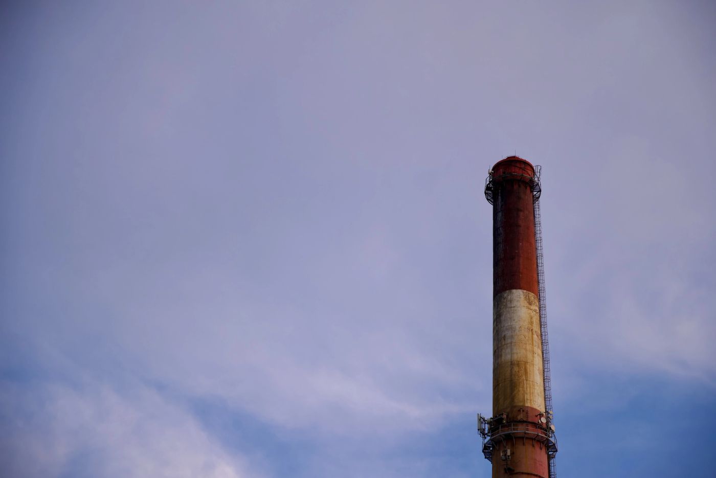 Smokestack in urban setting, on cloudy backdrop during golden hour.