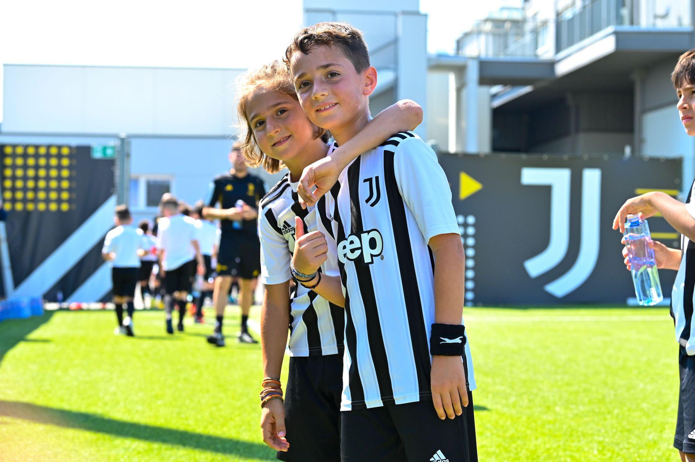 Two kids on the football pitch in black and white stripe jerseys with an arm around each other and a thumbs up
