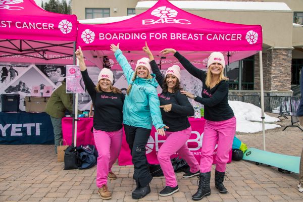 Women posing in front of a Boarding for Breast Cancer stall in hot pink pants