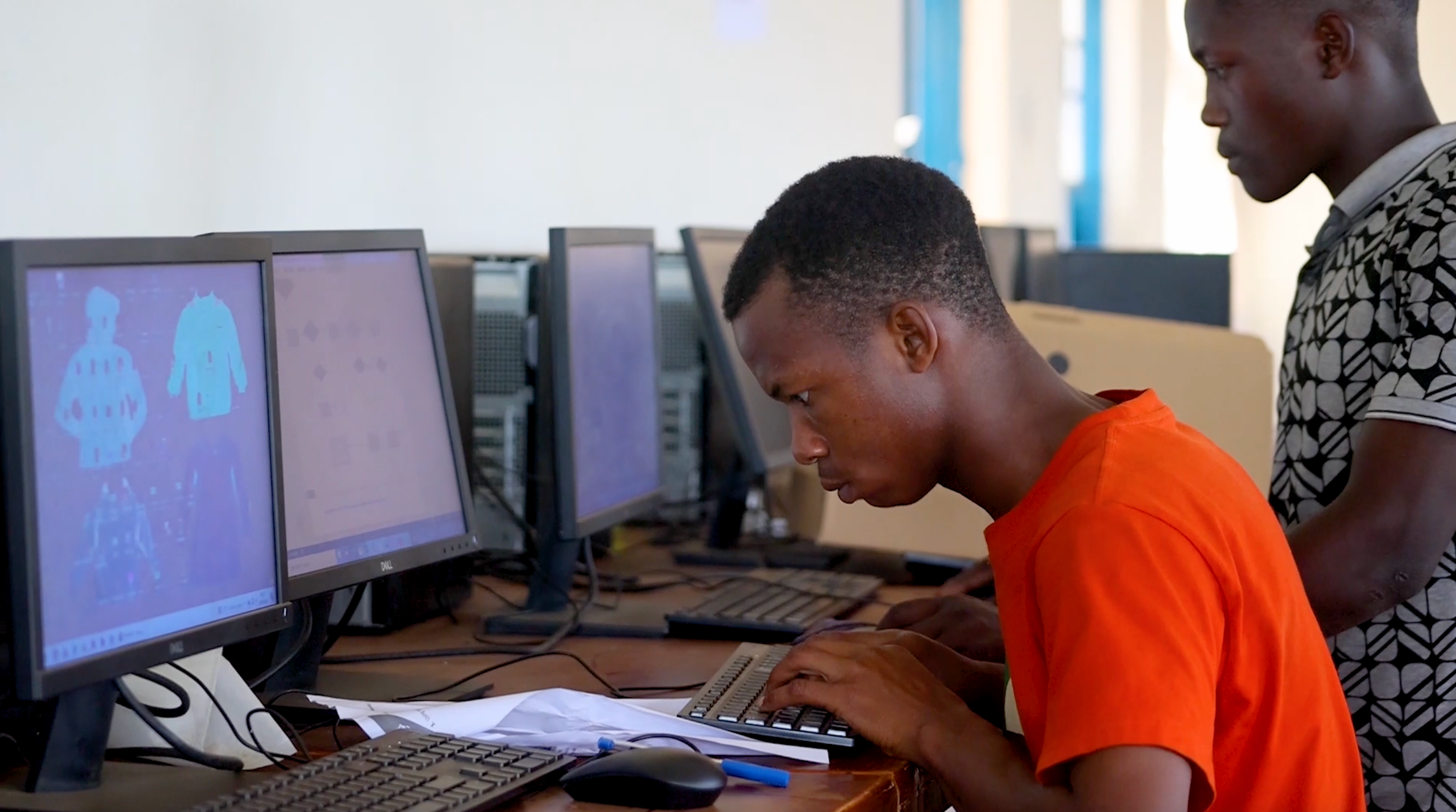 A high school student typing in front of some computer monitors