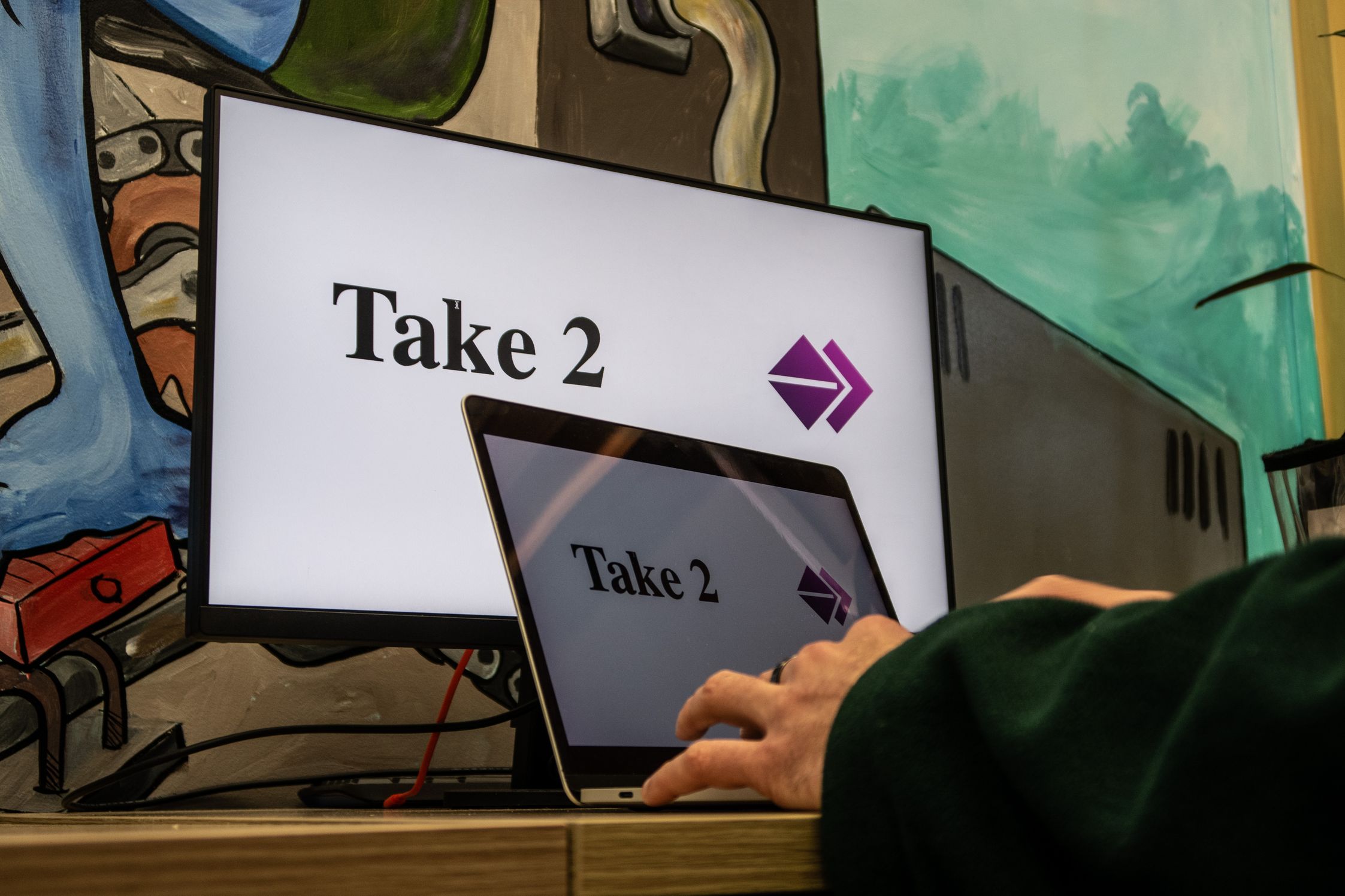 A laptop and desktop screen showing the Take2 logo