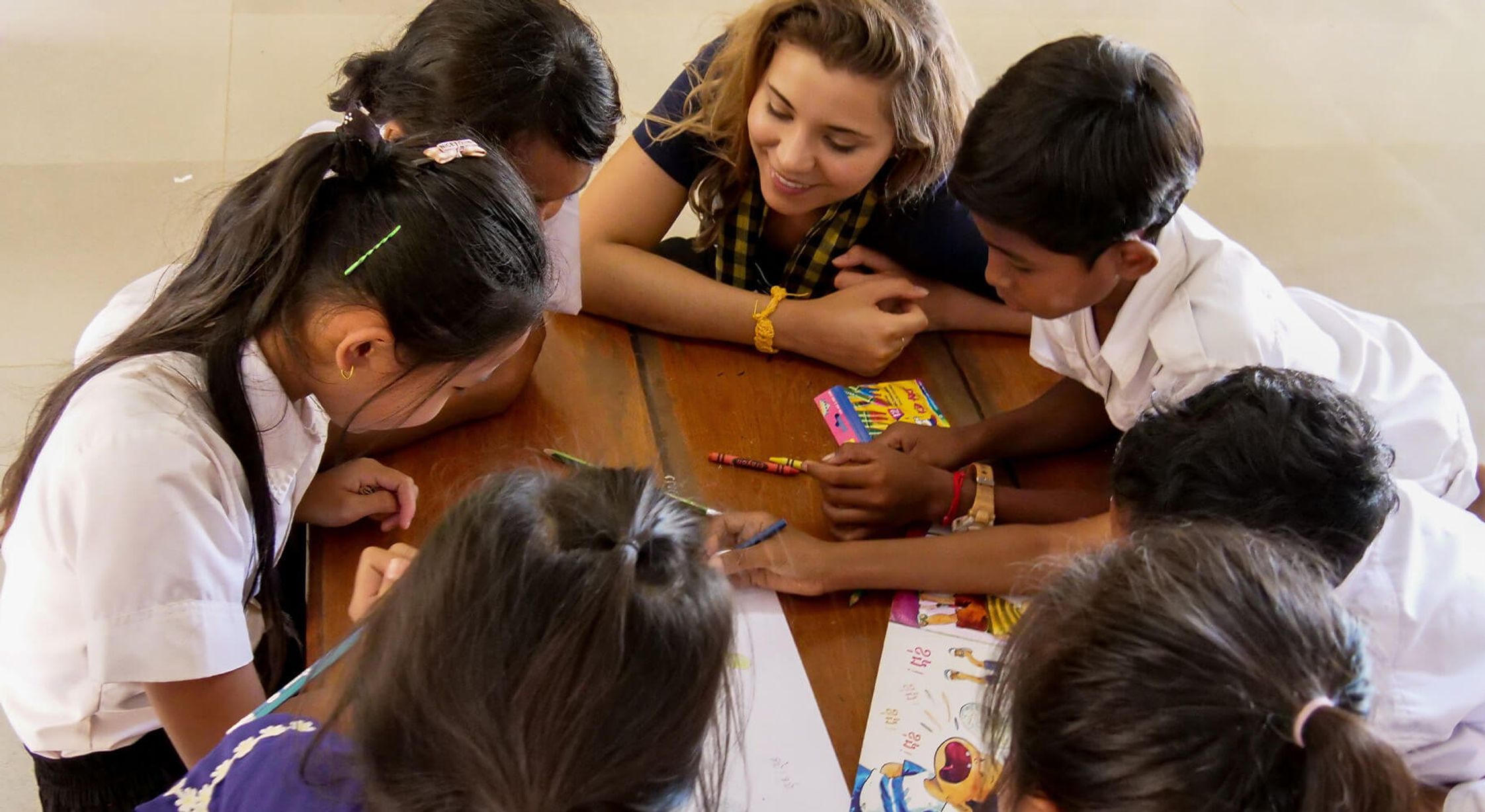 A group of kids and their teacher sitting around a table with books and crayons