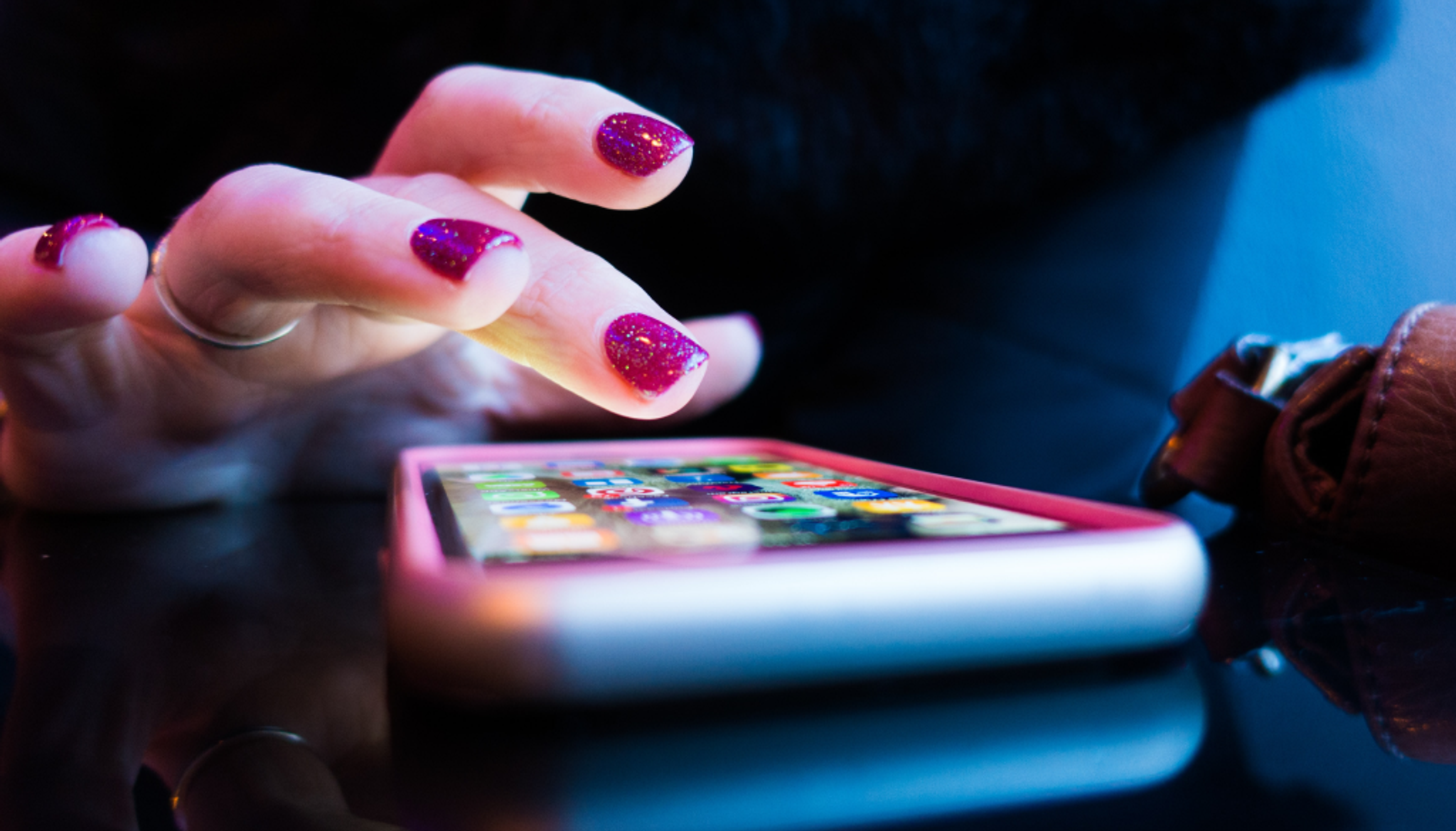 Hand with funky pink glitter nails tapping on a phone screen