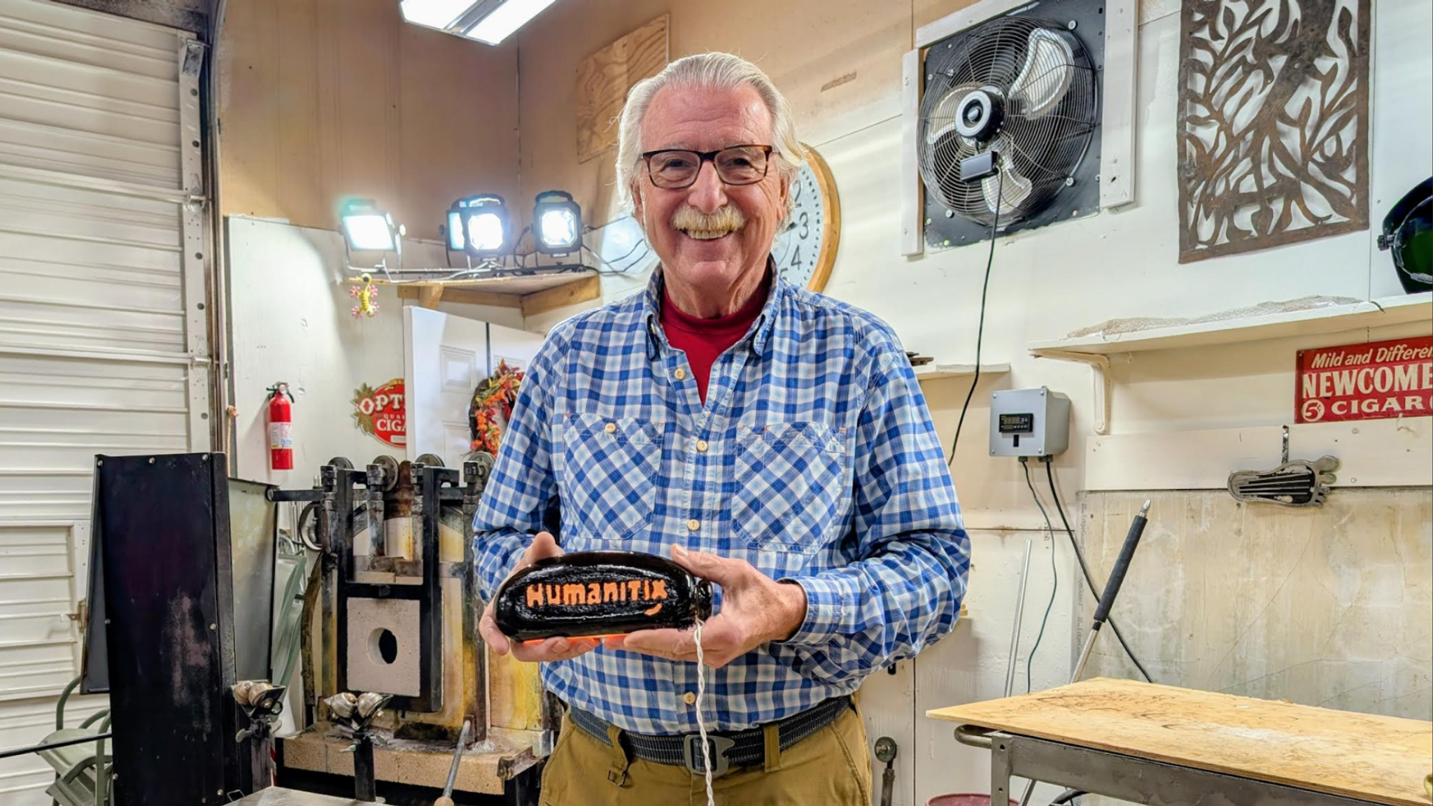 A photo of Larry smiling while holding the custom made glass-blown Humanitix lamp
