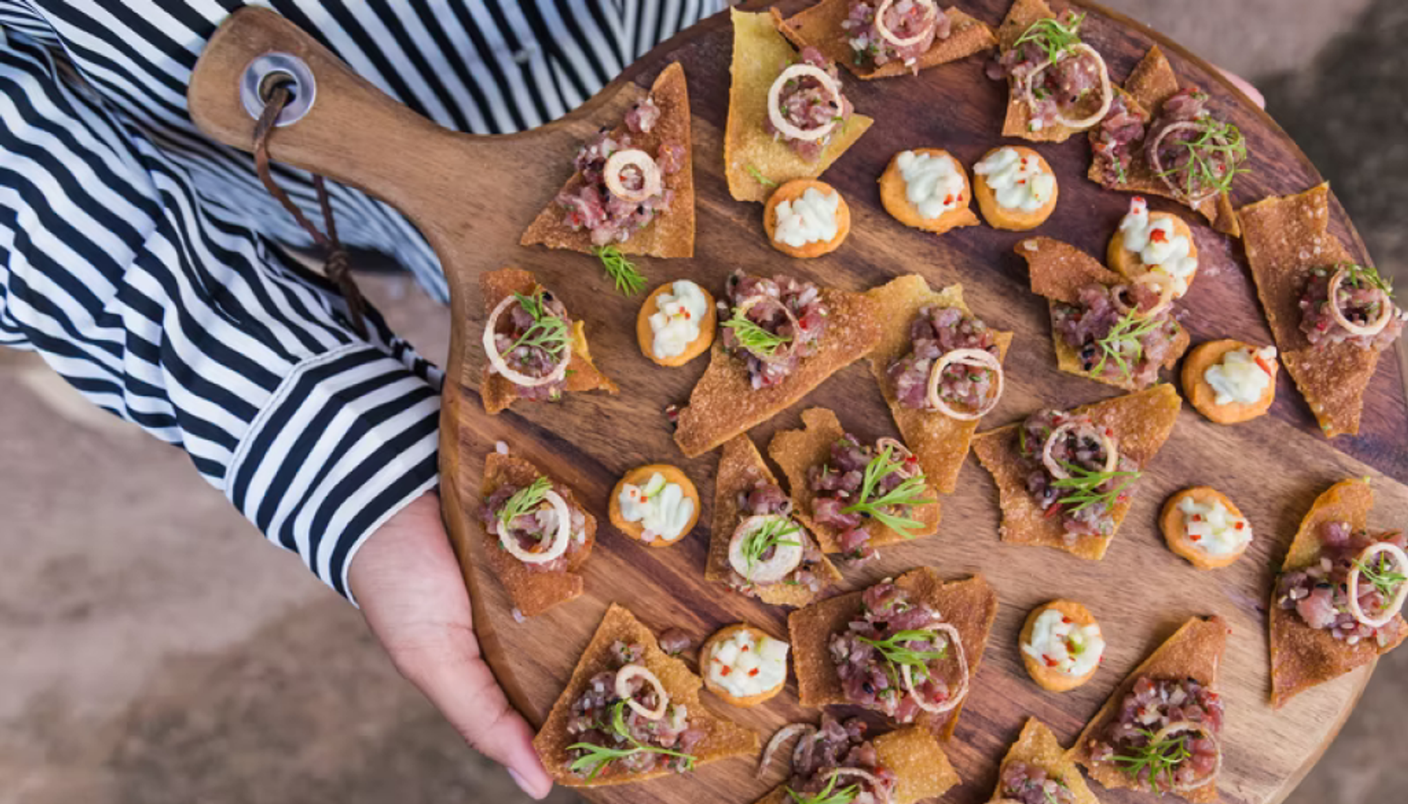 A pair of hands holding a wonderful array of food on a platter for an event.