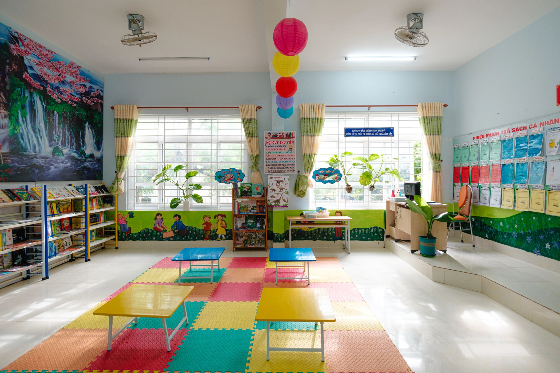 A clean, bright and colourful interior of a library filled with books, decorations, tables and floor mats