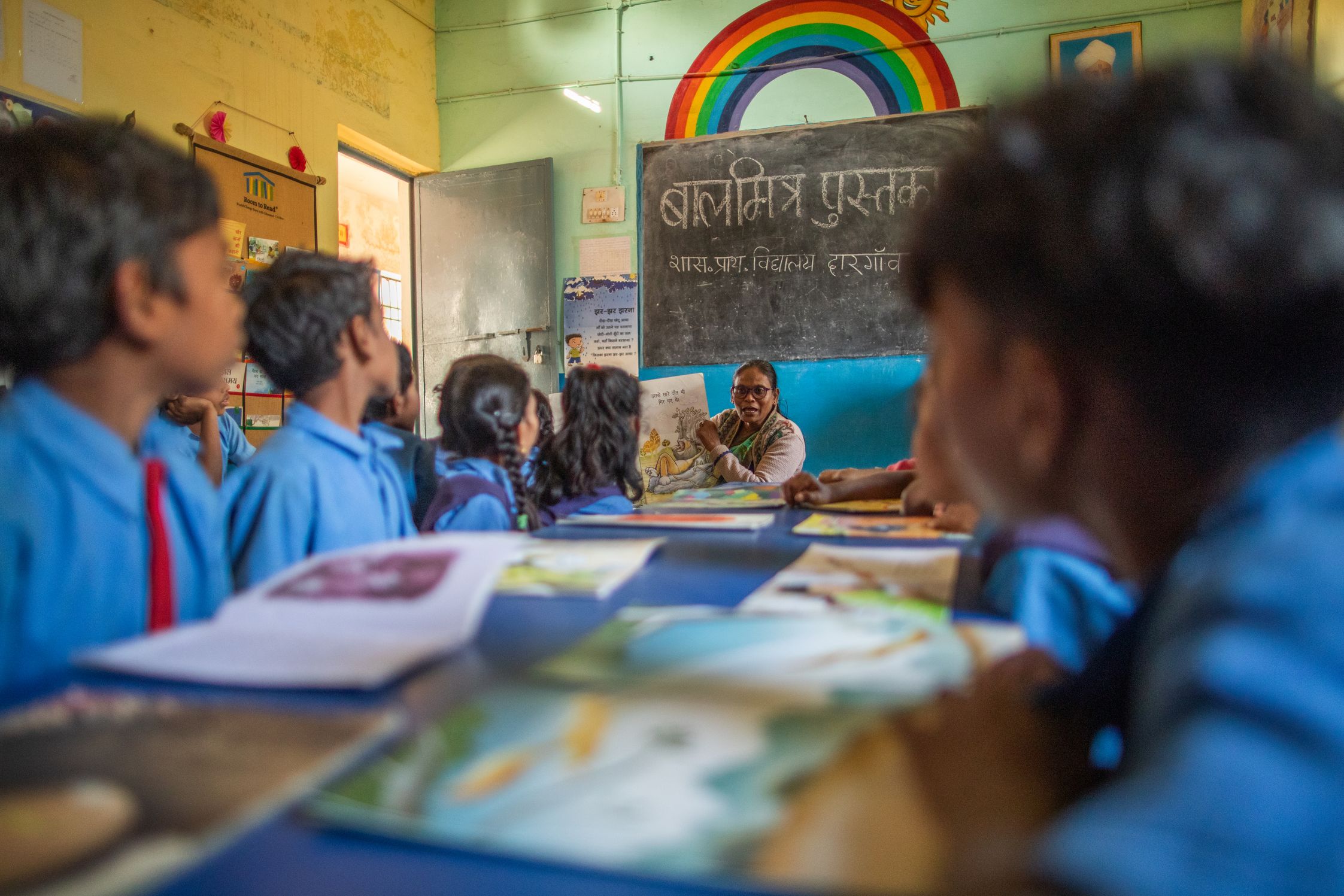 A teacher reading a picture book to students in India with a chalkboard in the background