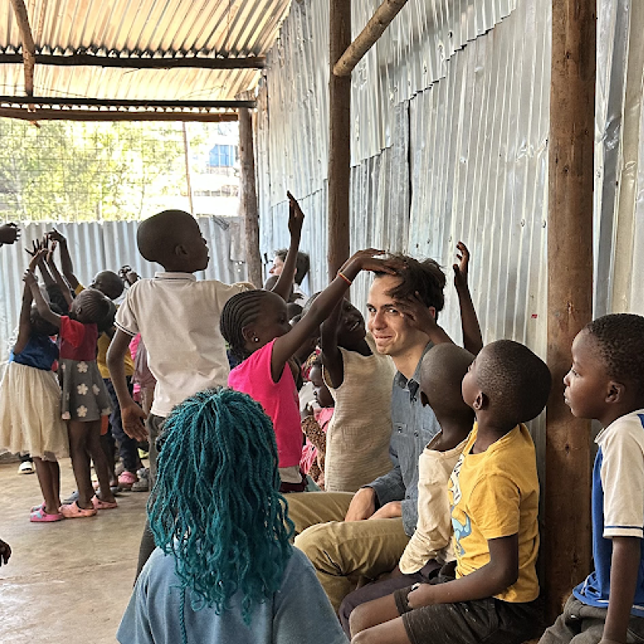 A photo of Nathan smiling at the camera surrounded by Tanzanian kids touching his hair