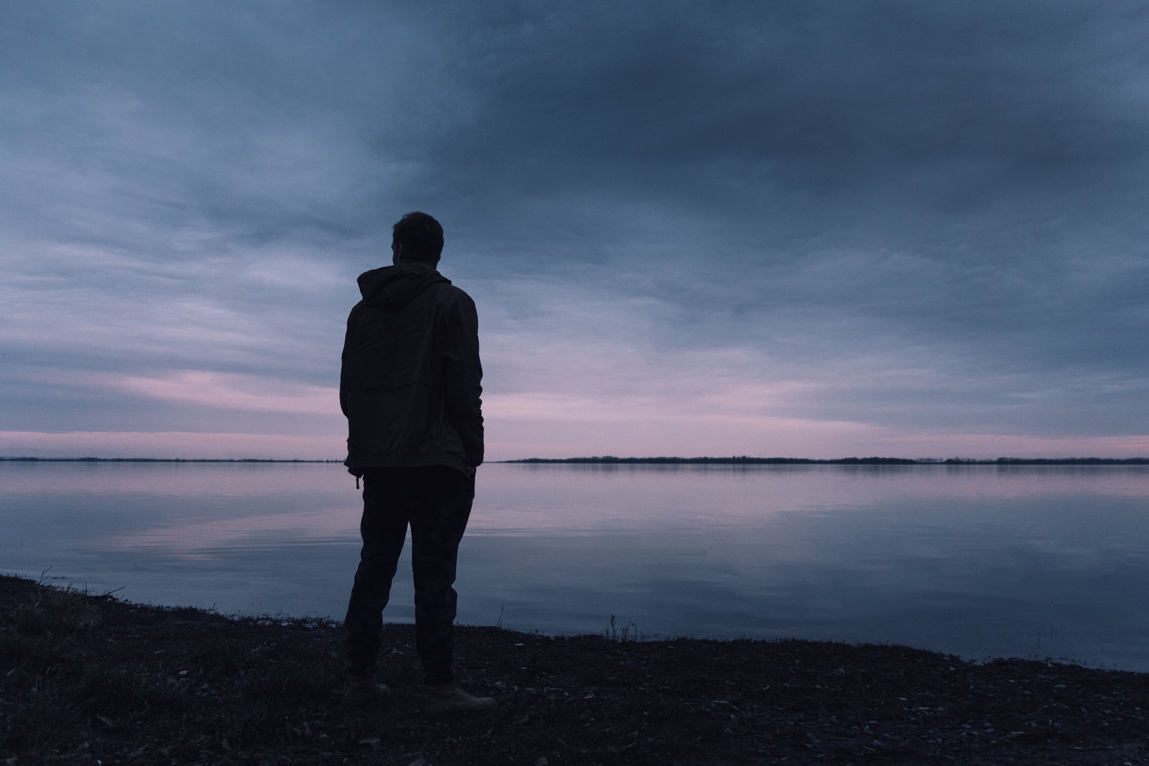 Man contemplating while looking our over a lake at twilight