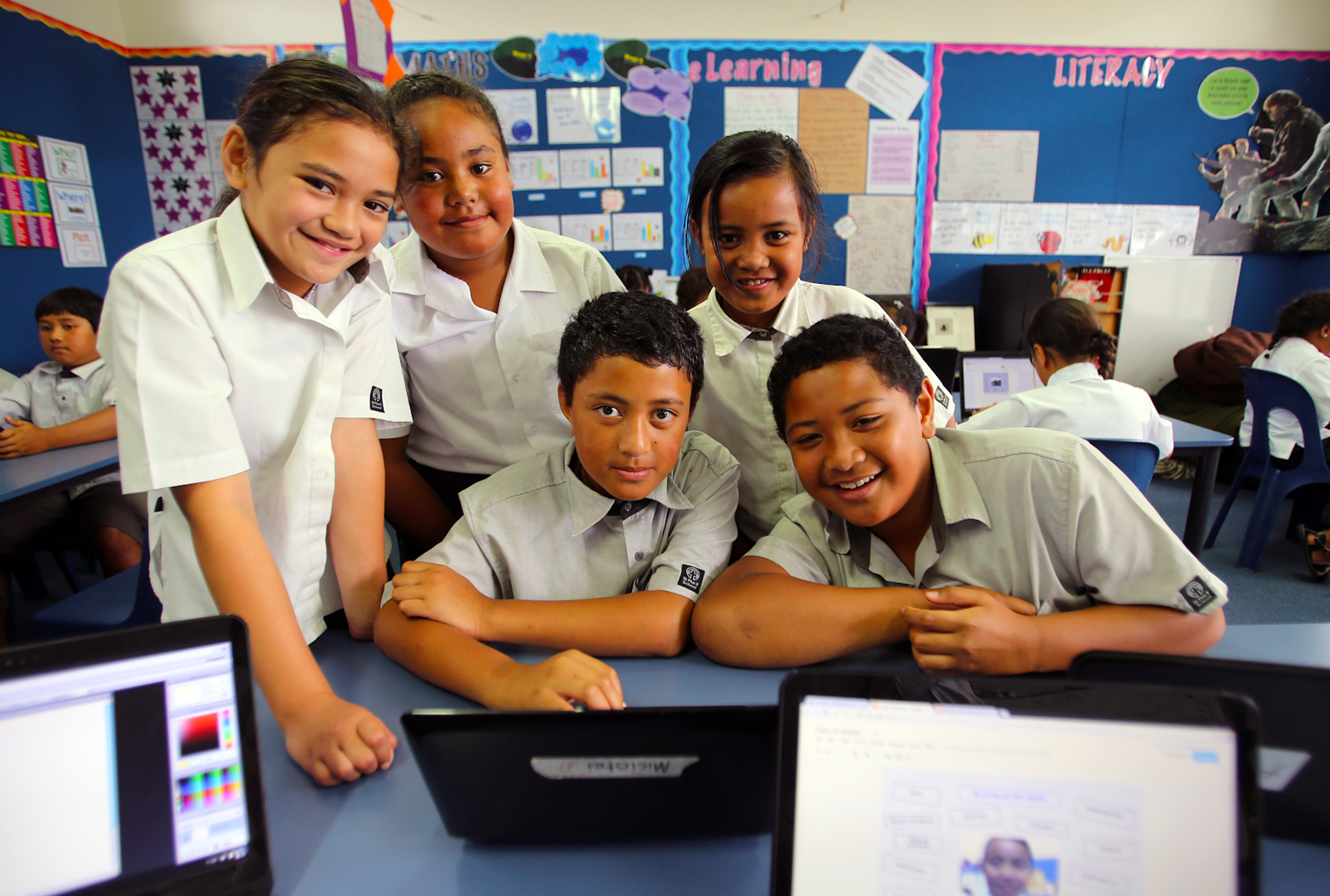 Students of Manaiakalani smiling gathered around a desk with laptops