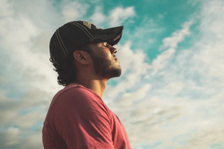 Man in a baseball cap breathes deeply in front of a blue sky.