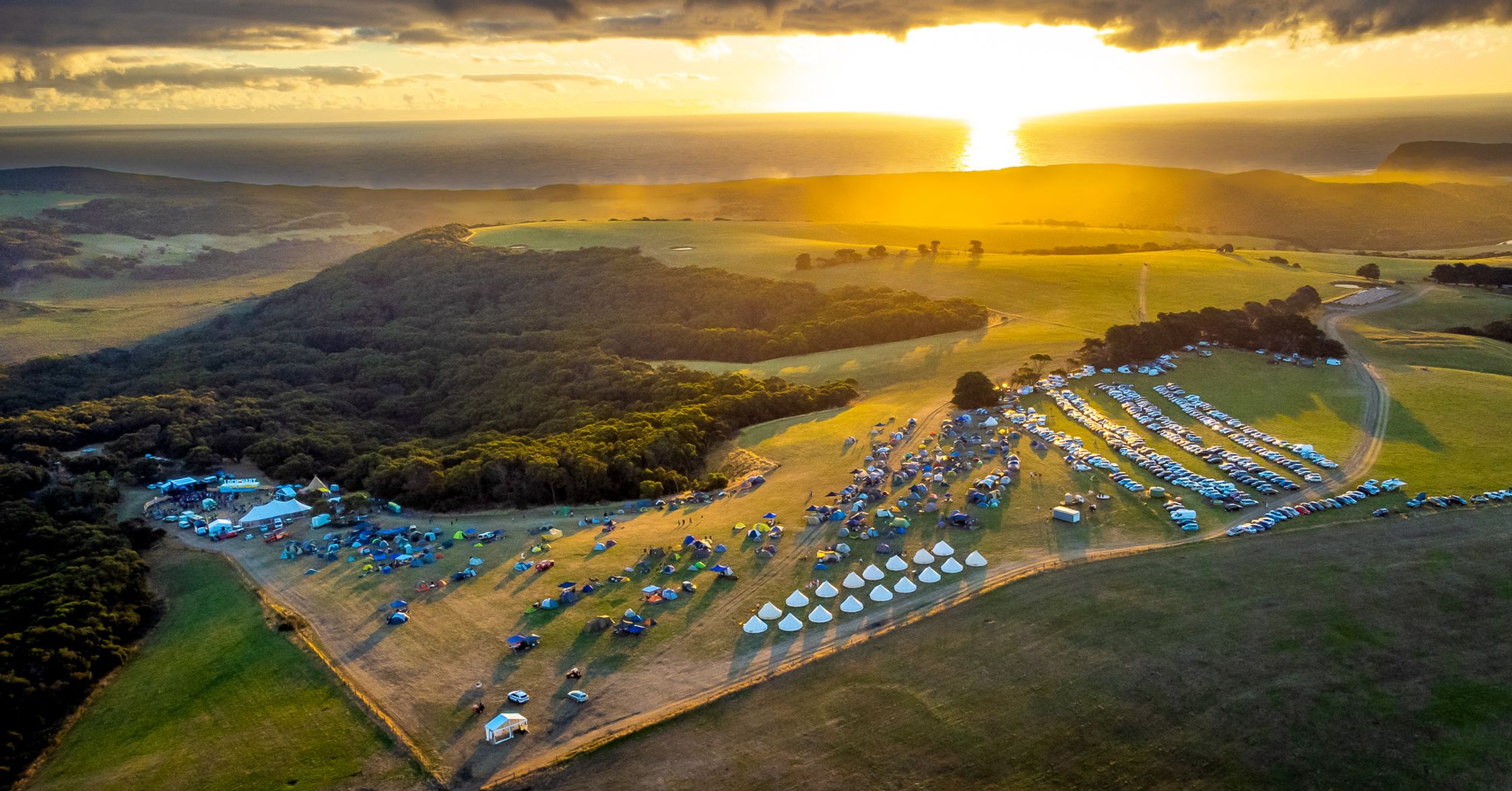 A bird's eye view of the Loch Hart festival site on green fields with the sunset in the background