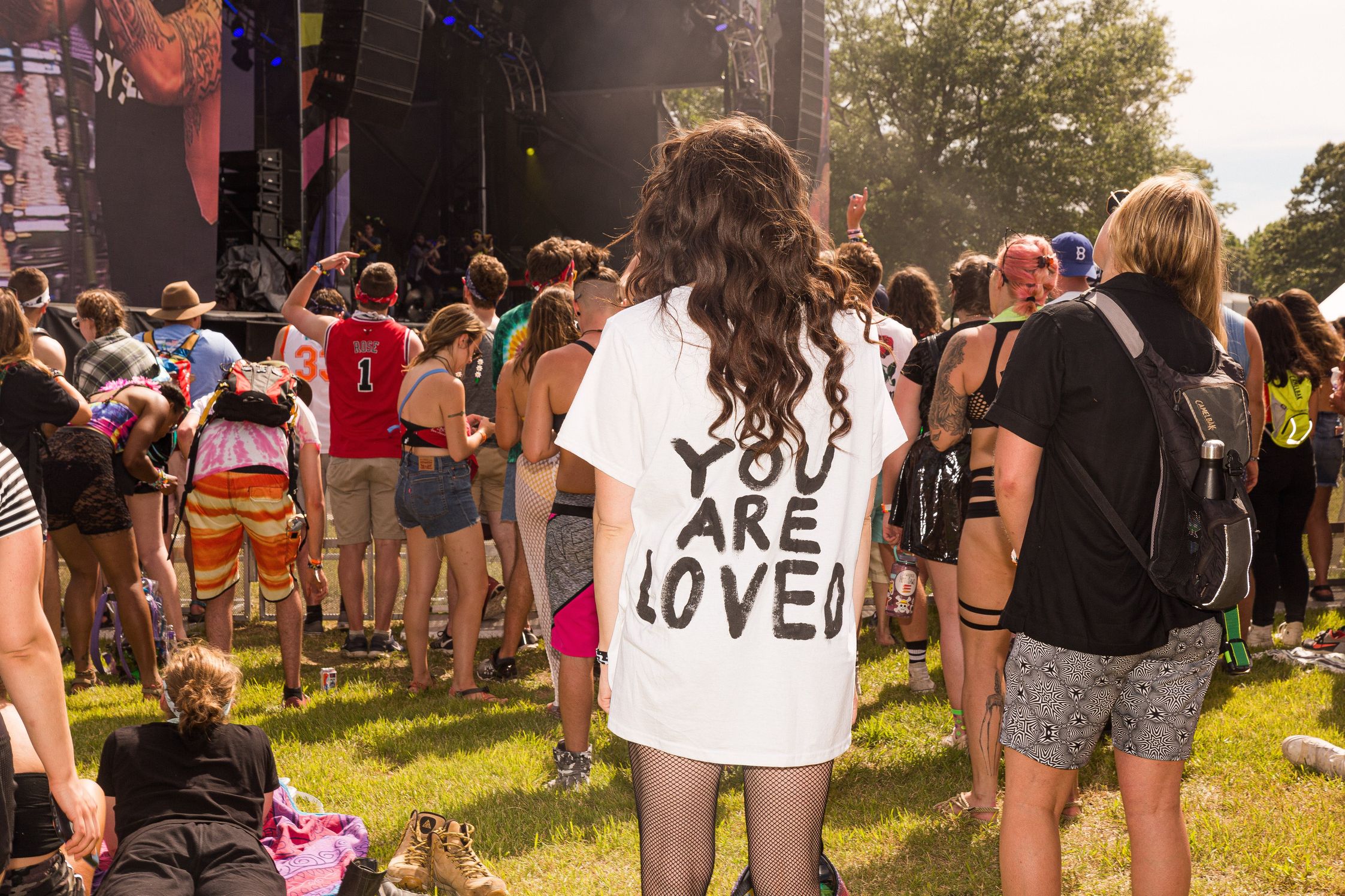 A festival-goer with the words 'you are loved' in black on the back of their white tshirt 