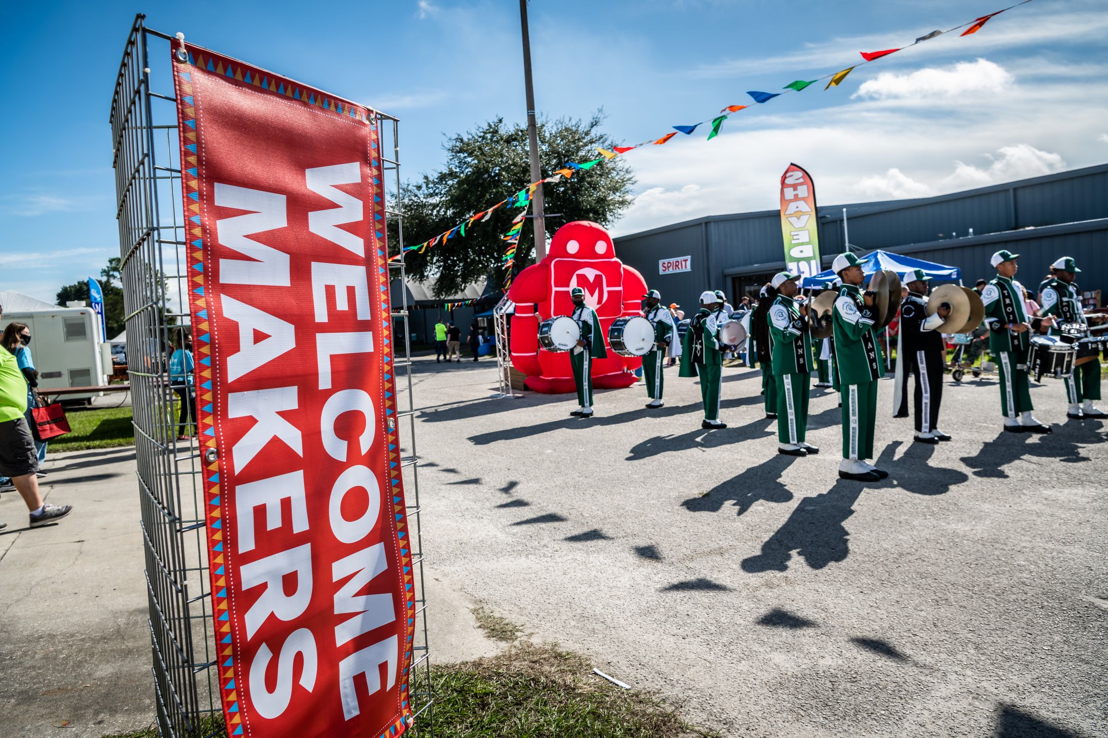 Welcome Makers red banner in the foreground with marching band