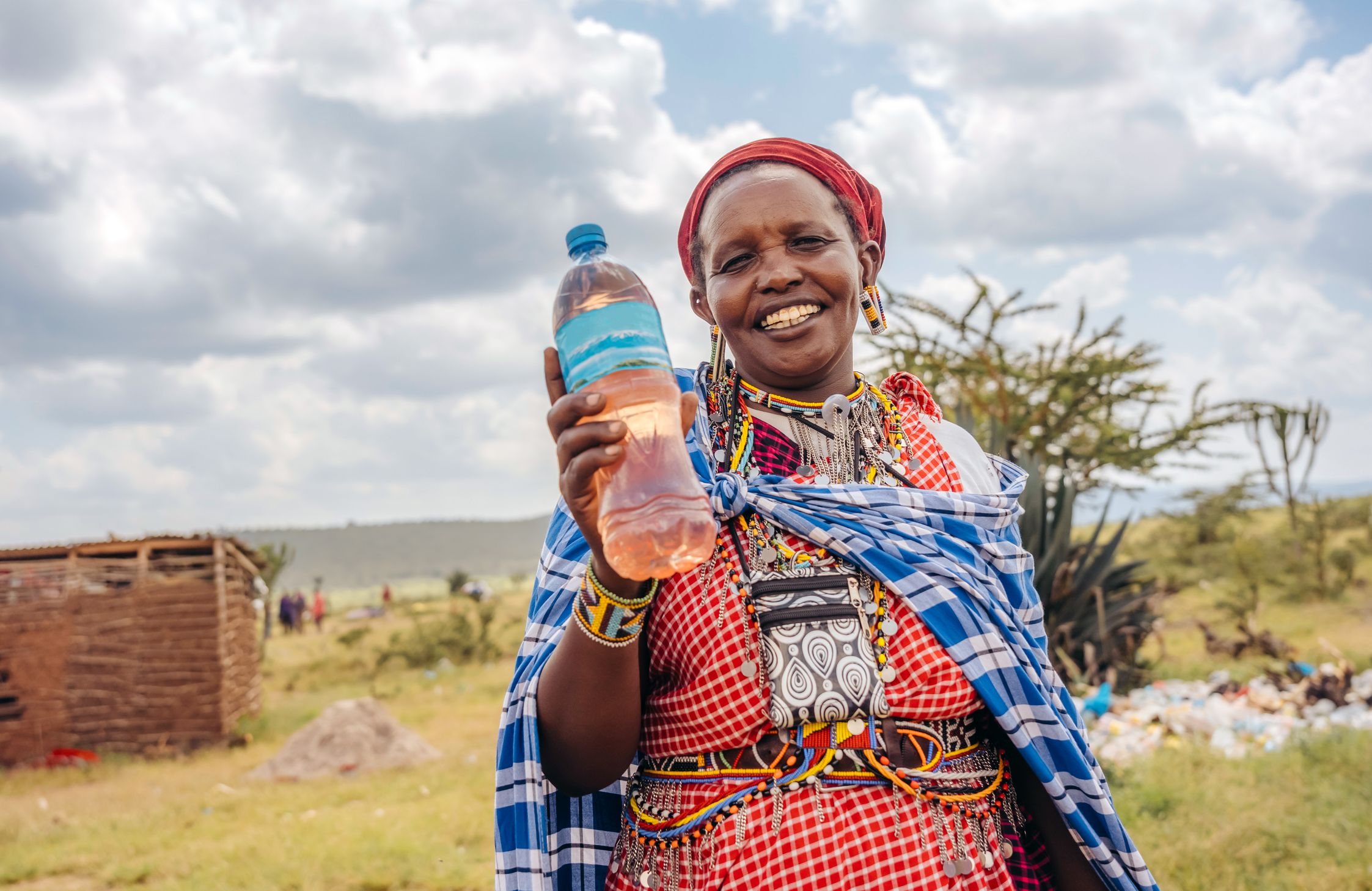 A woman in colourful headscarf and dress holding a bottle of water while smiling