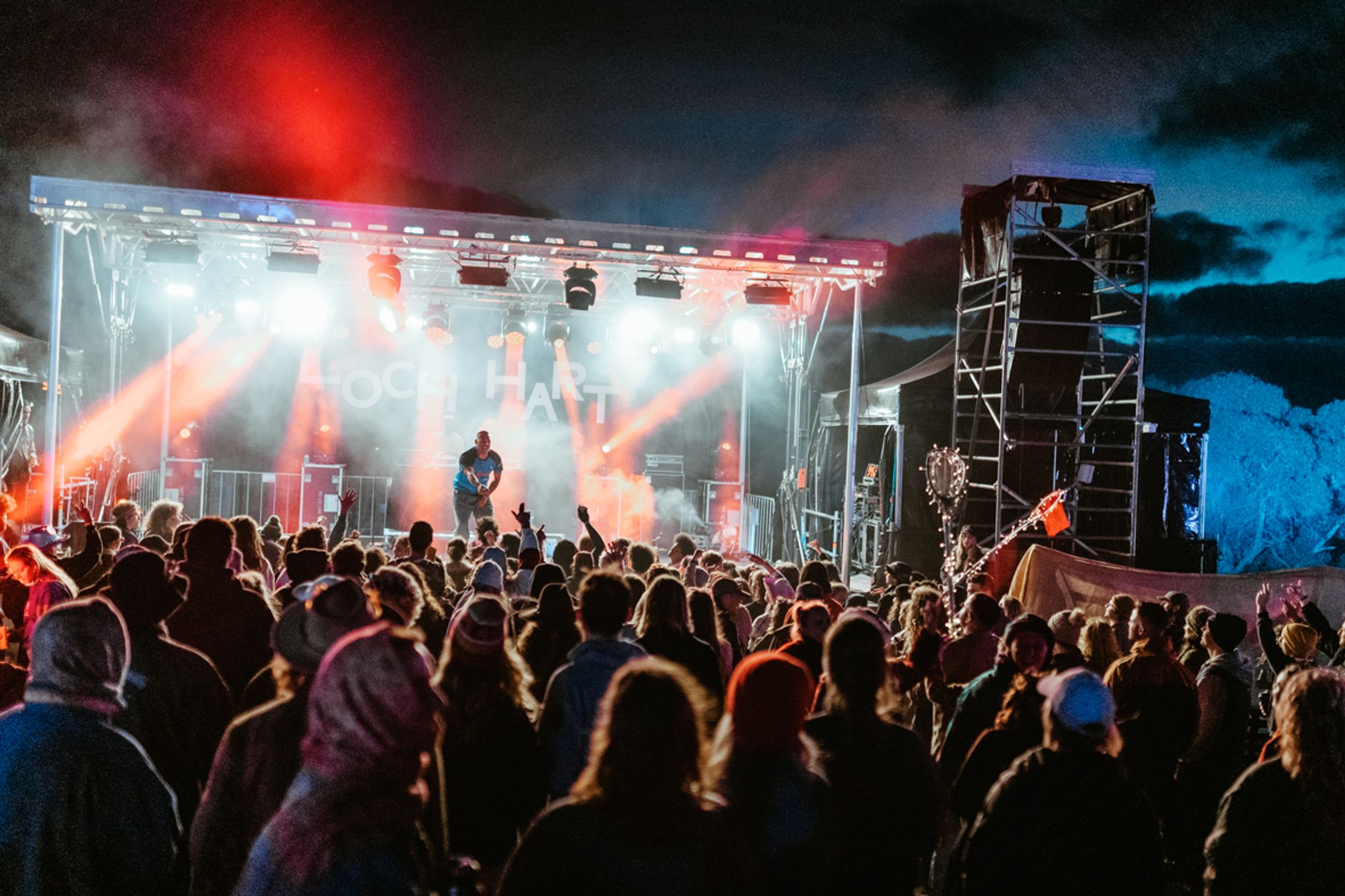 An artist performs on the Loch Hart stage at night lit up with red and white lights