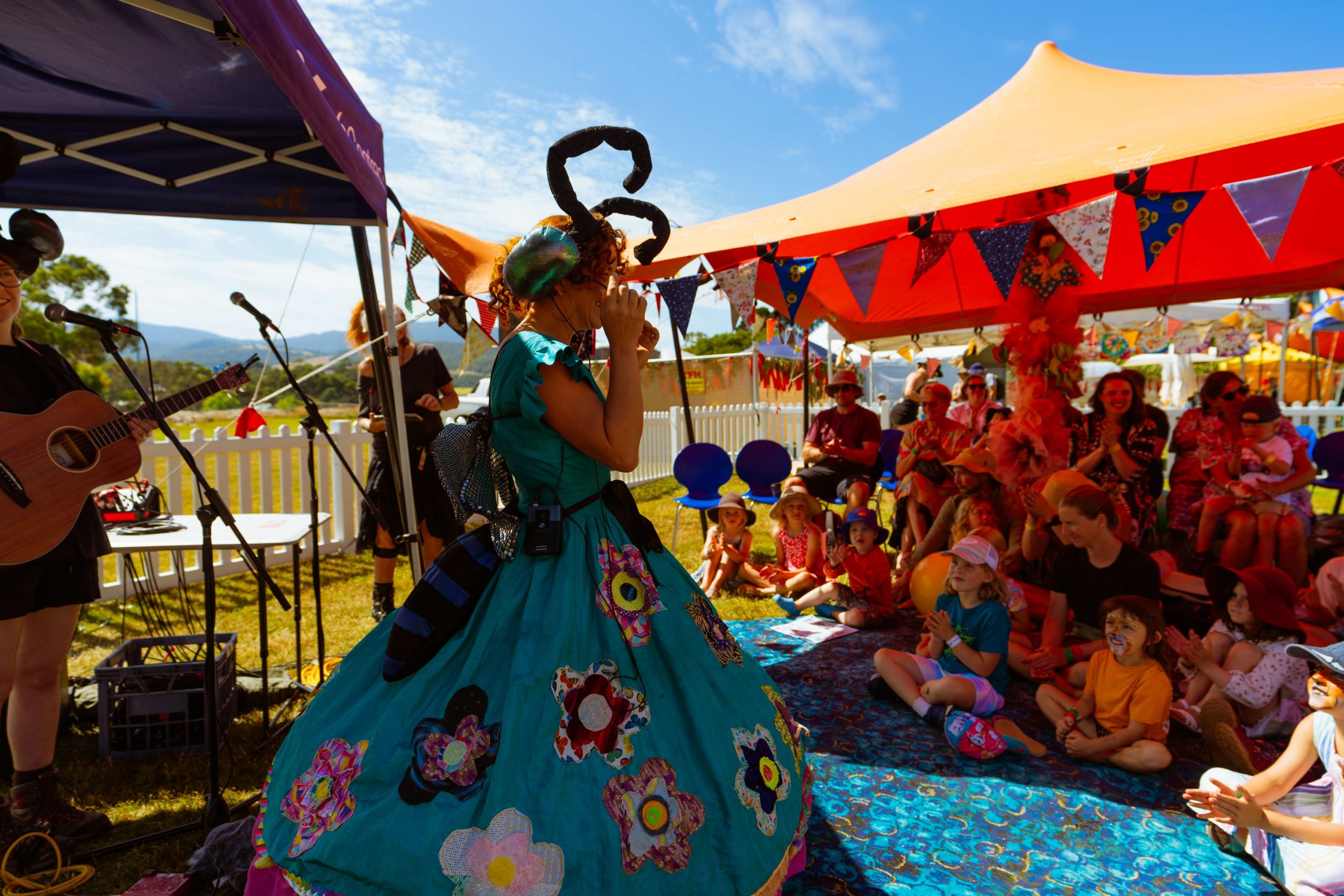 A woman dressed in colourful clothes and festival attendees under an orange marquee