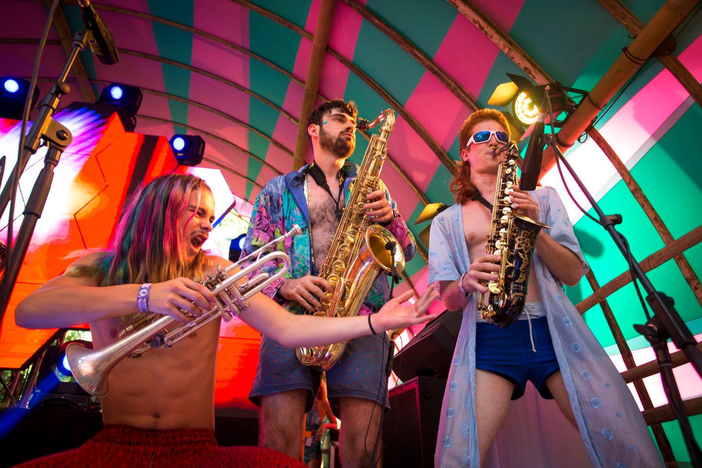 Musicians playing trumpet and saxaphones on stage with a colourful backdrop