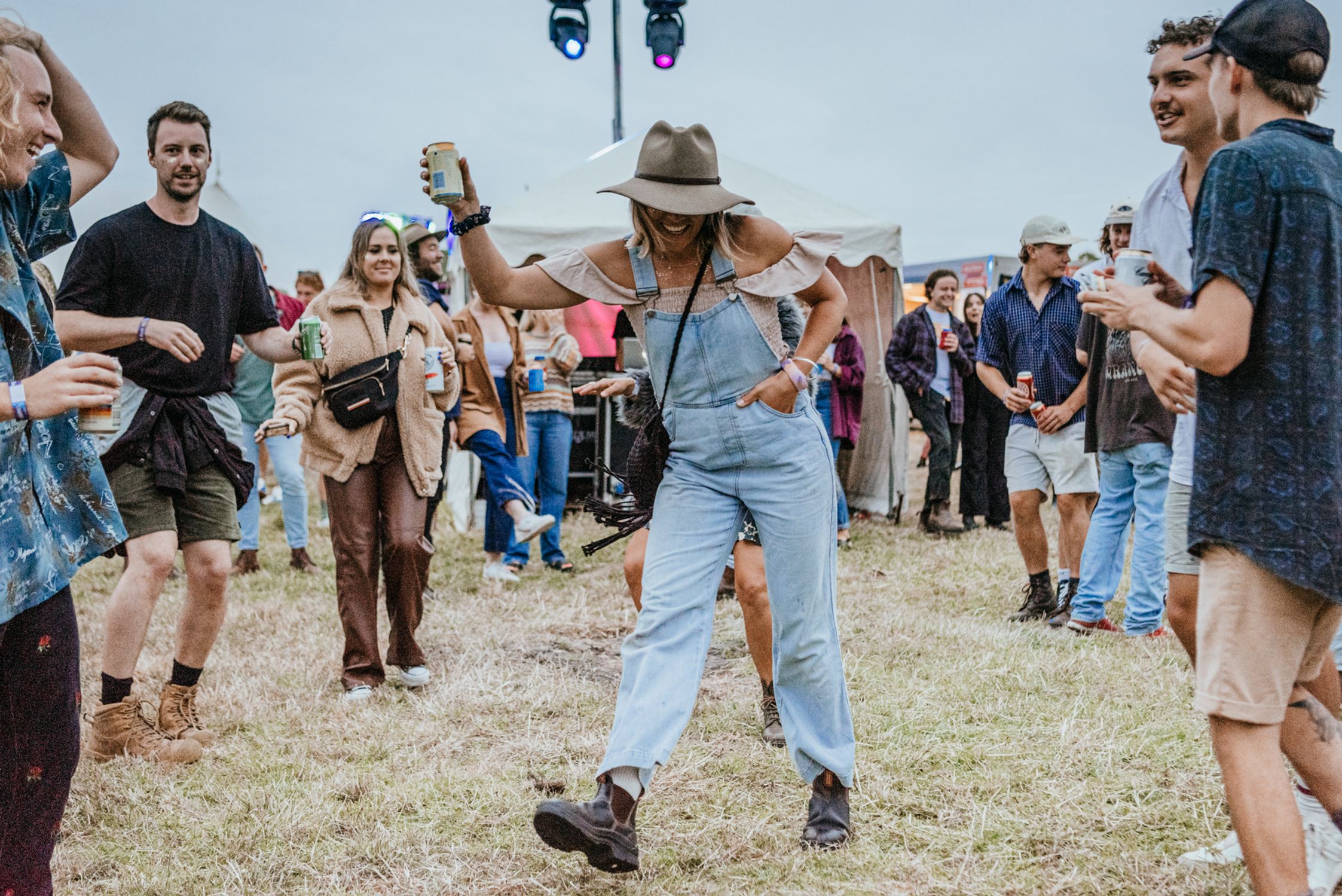 A woman in denim ovrealls dancing with a beer in hand on the festival site