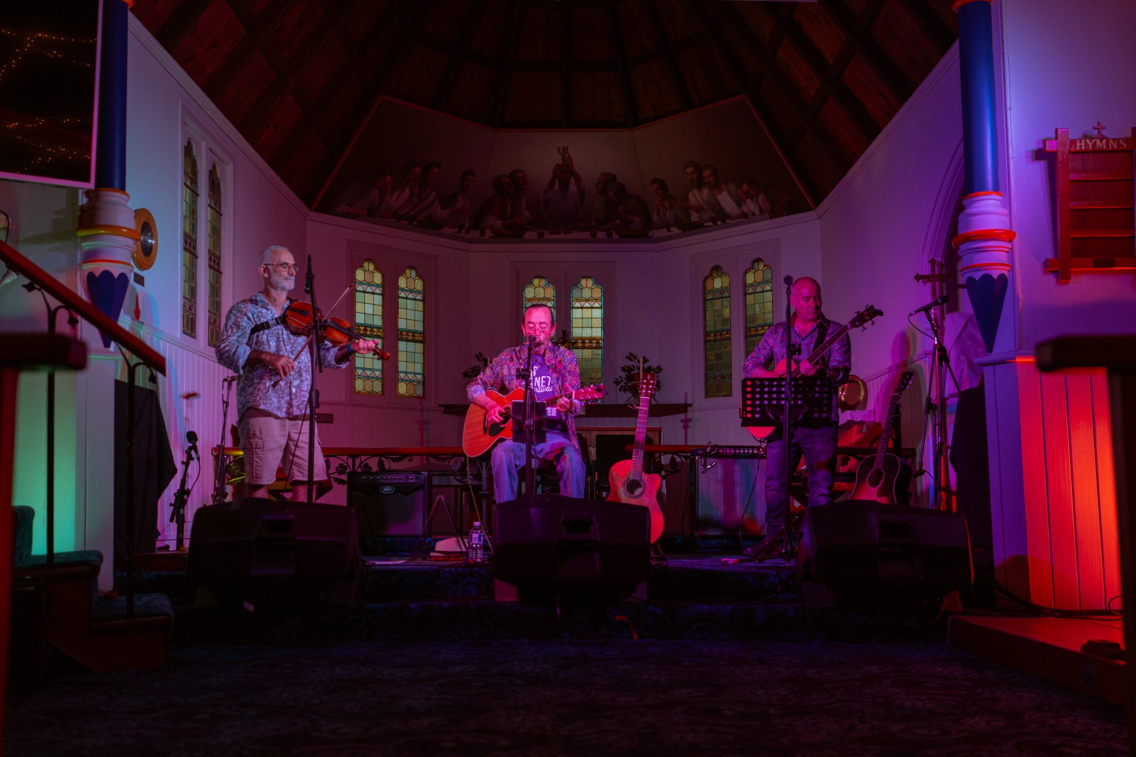 A moodily lit stage with a violinist and two guitarists performing