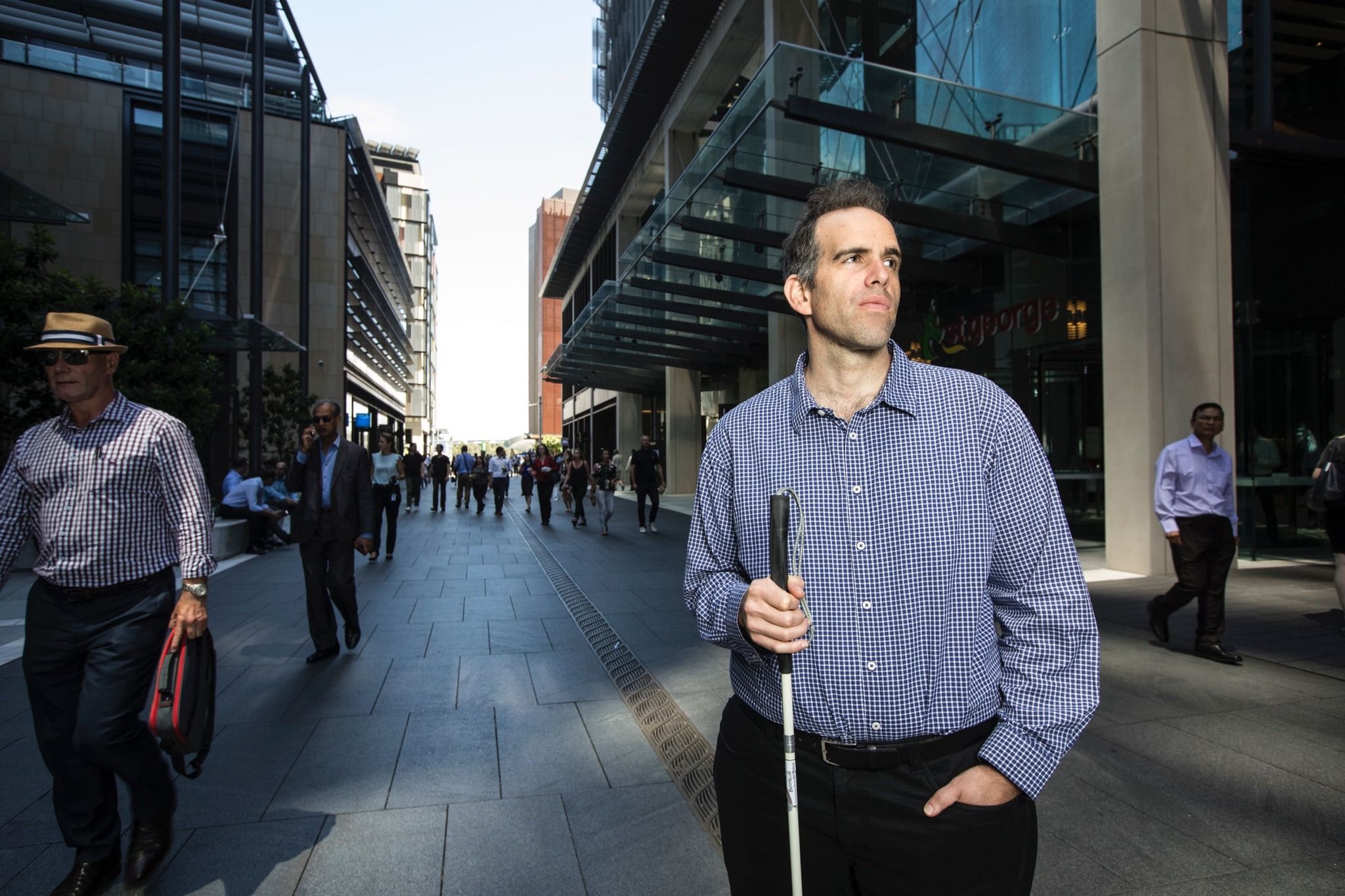 A picture of Rocco standing in the CBD holding a walking cane and with a hand in his pocket.