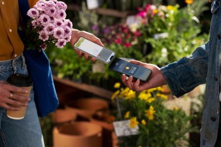 A person taking a contactless payment using their iPhone against a floral backdrop