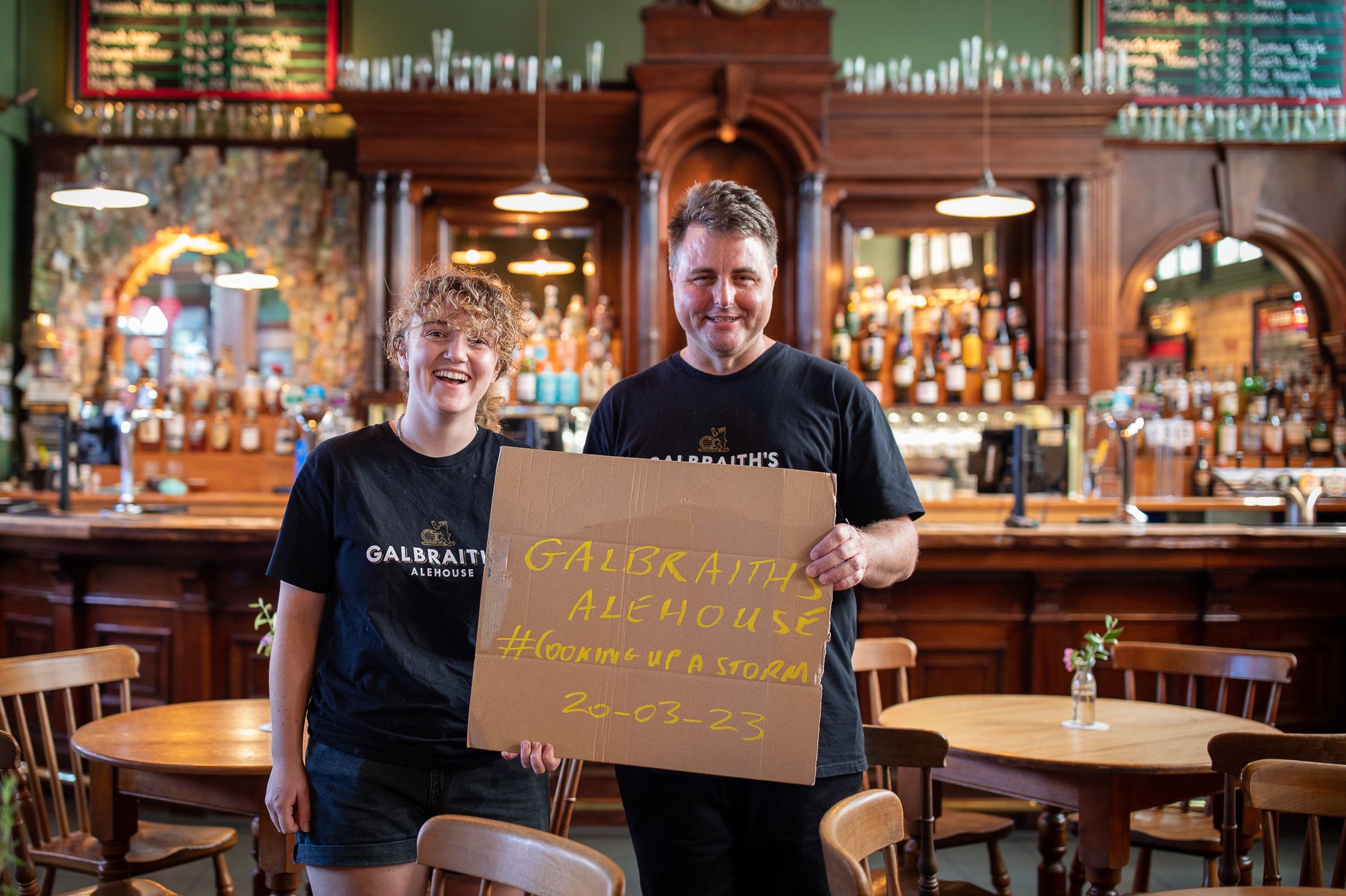 Staff holding cardboard sign saying Galbraiths Alehouse #coockingupastorm 20-03-23