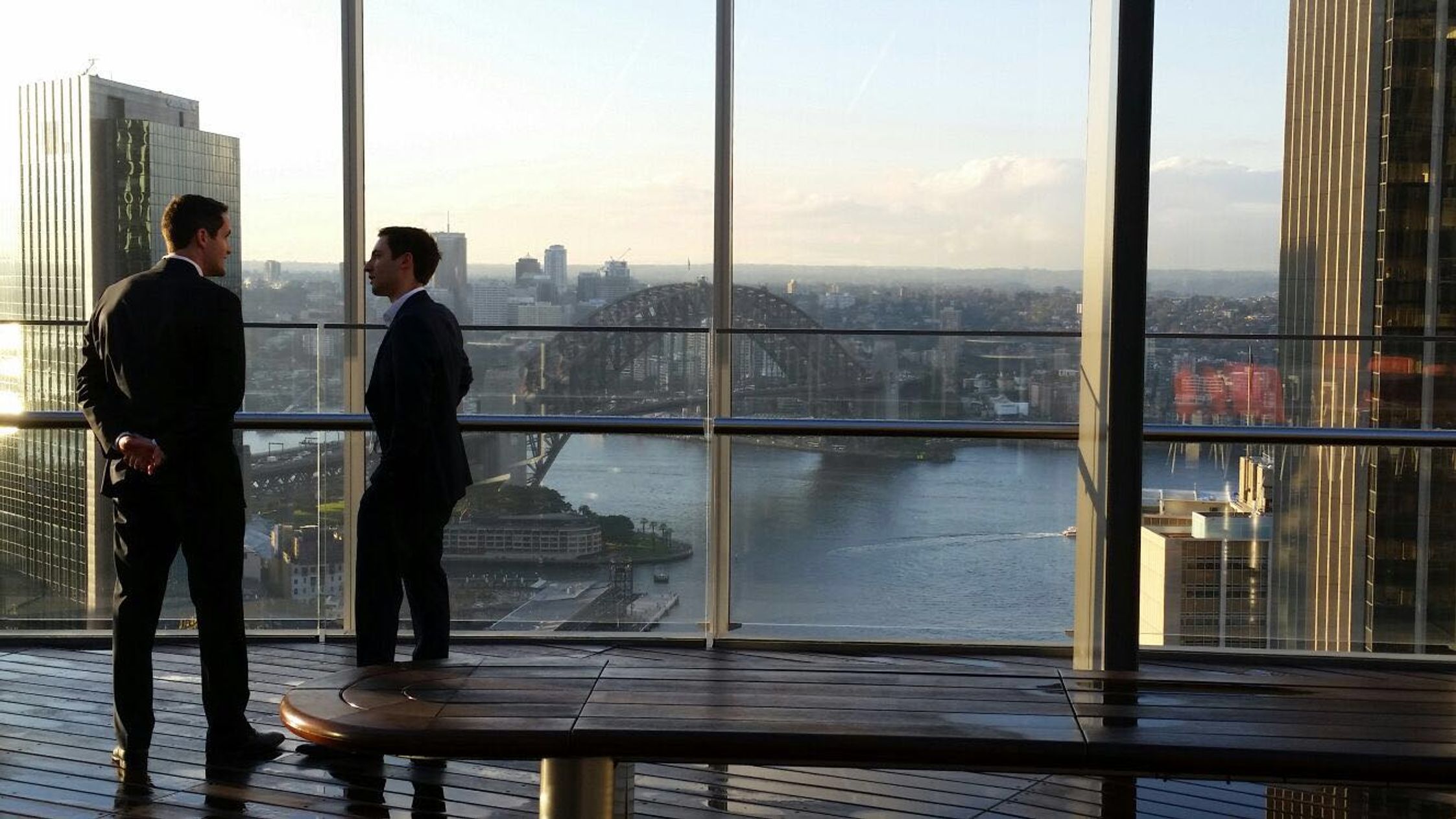 Adam and Josh in suits at the Bloomberg Rooftop overlooking the Sydney Harbour