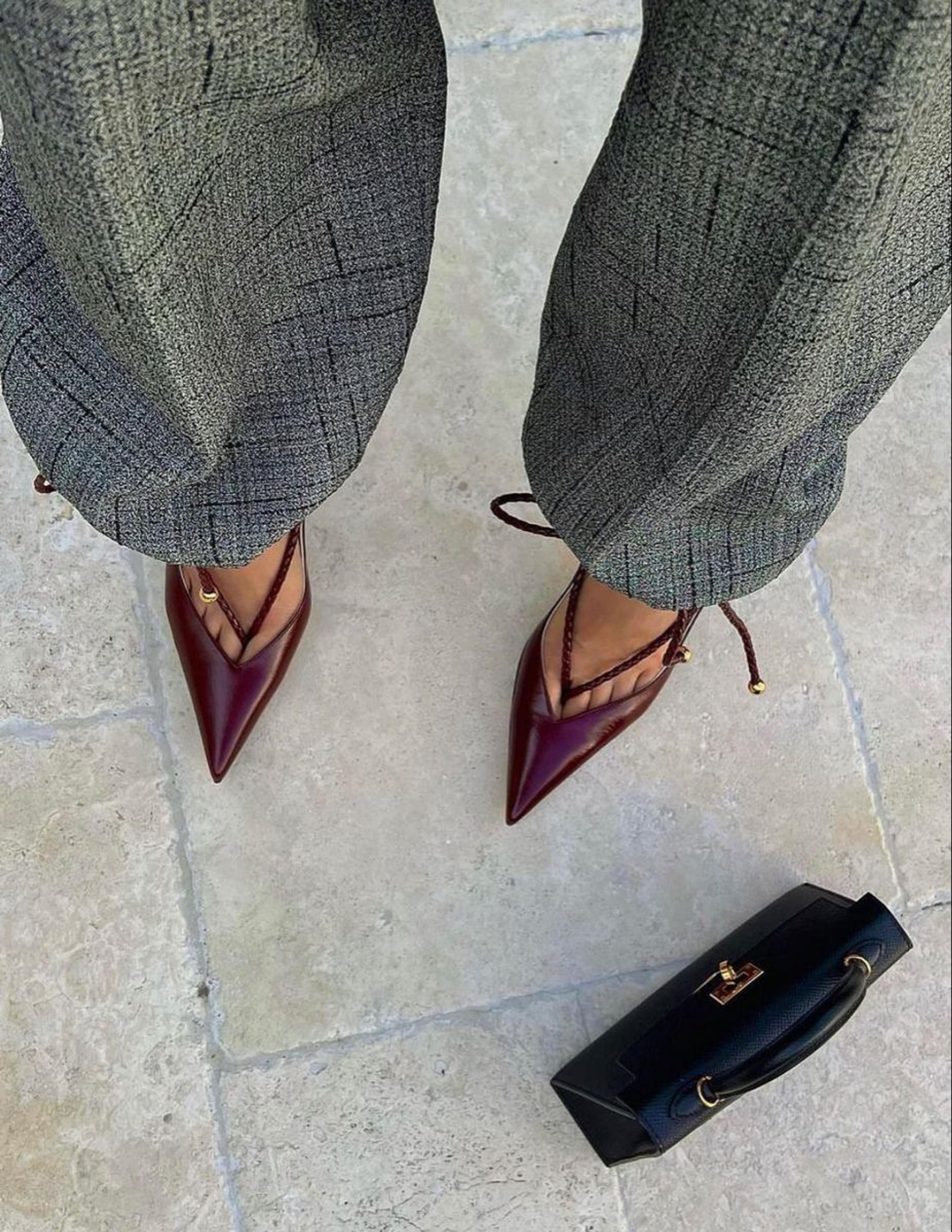 Burgundy pointed slingback heels with tweed wide-leg trousers and a black top-handle bag on stone paving