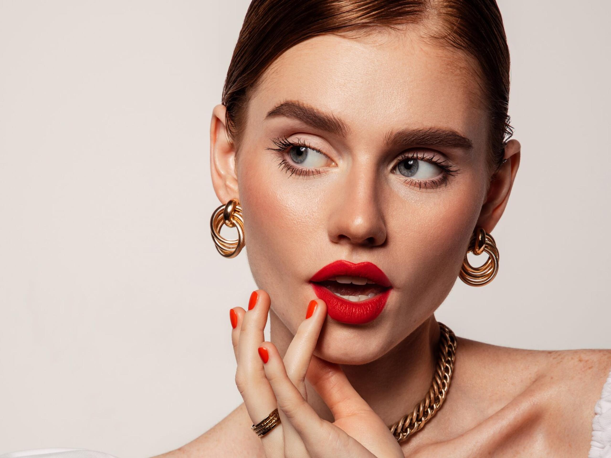 Beauty portrait with a bold red lip, red nails and gold hoop earrings