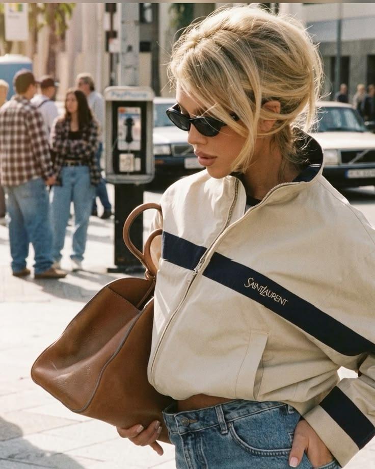 Woman in a cream track jacket and sunglasses with a tan leather tote