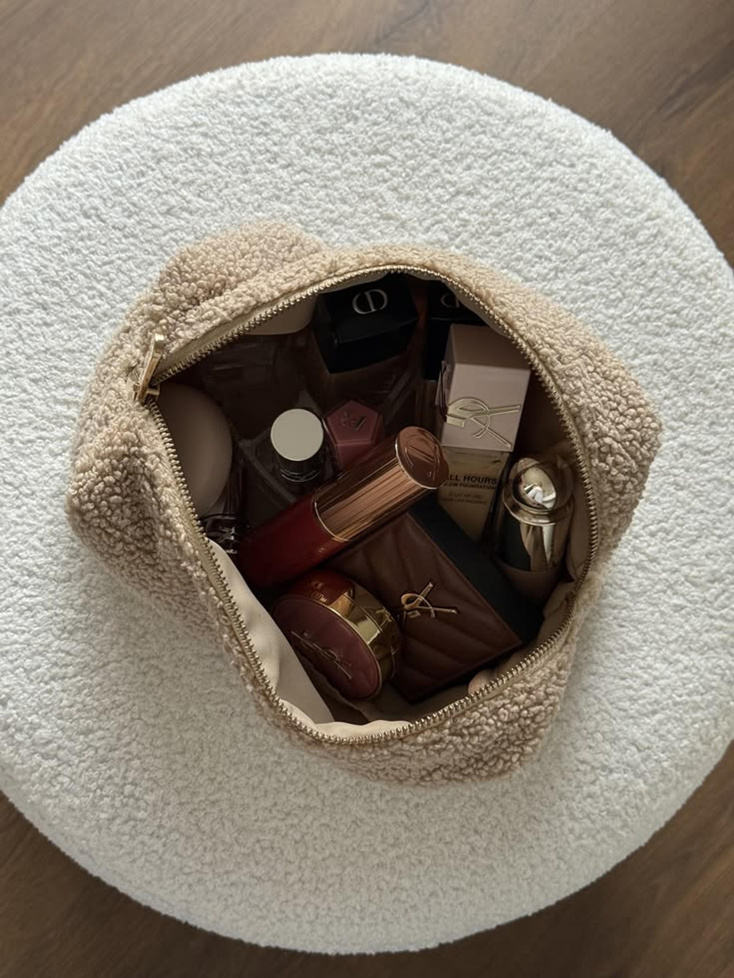 Cream teddy make-up bag filled with lipsticks, compacts and perfume on a boucle stool