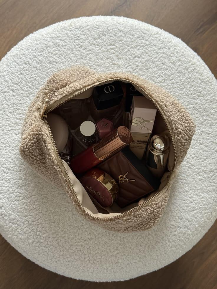 Cream teddy make-up bag filled with lipsticks, compacts and perfume on a boucle stool