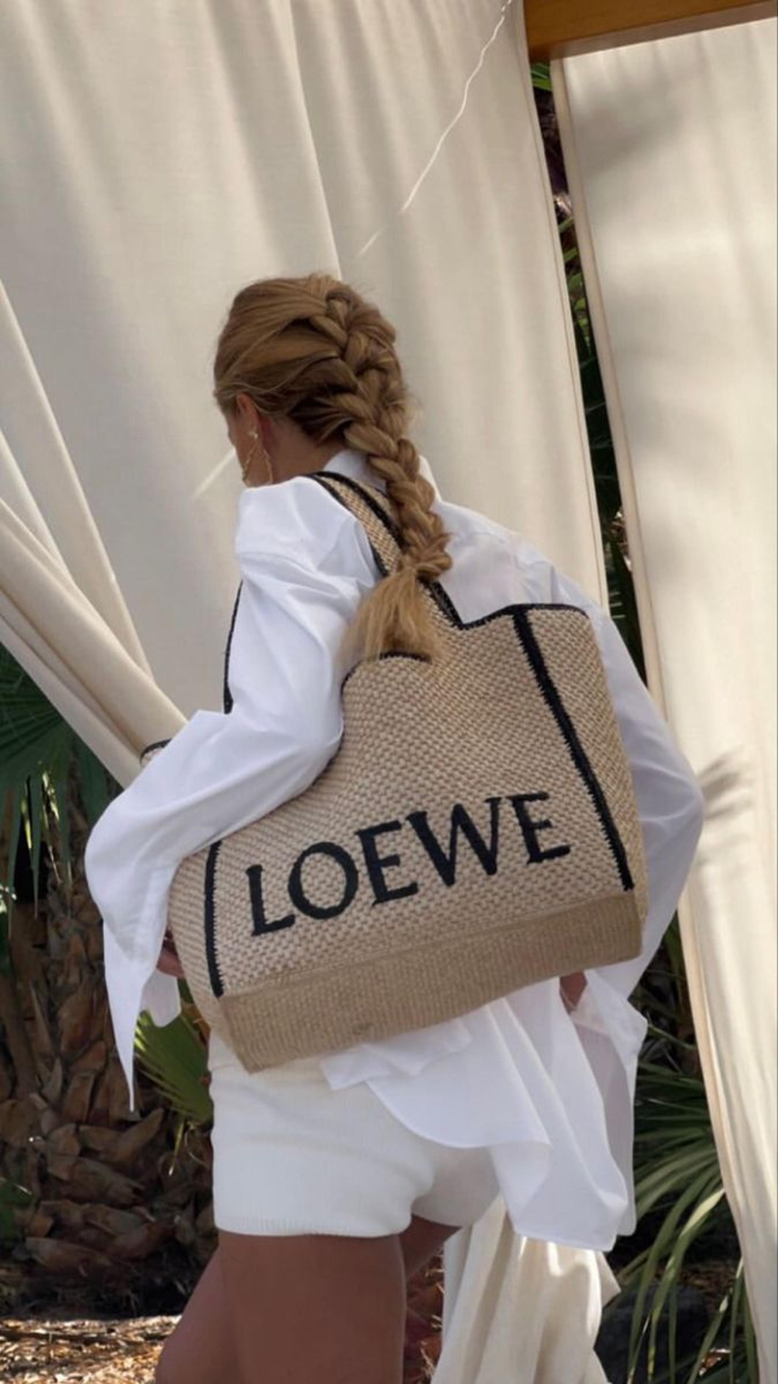 Woman with a long braid carrying a Loewe raffia tote over a white shirt