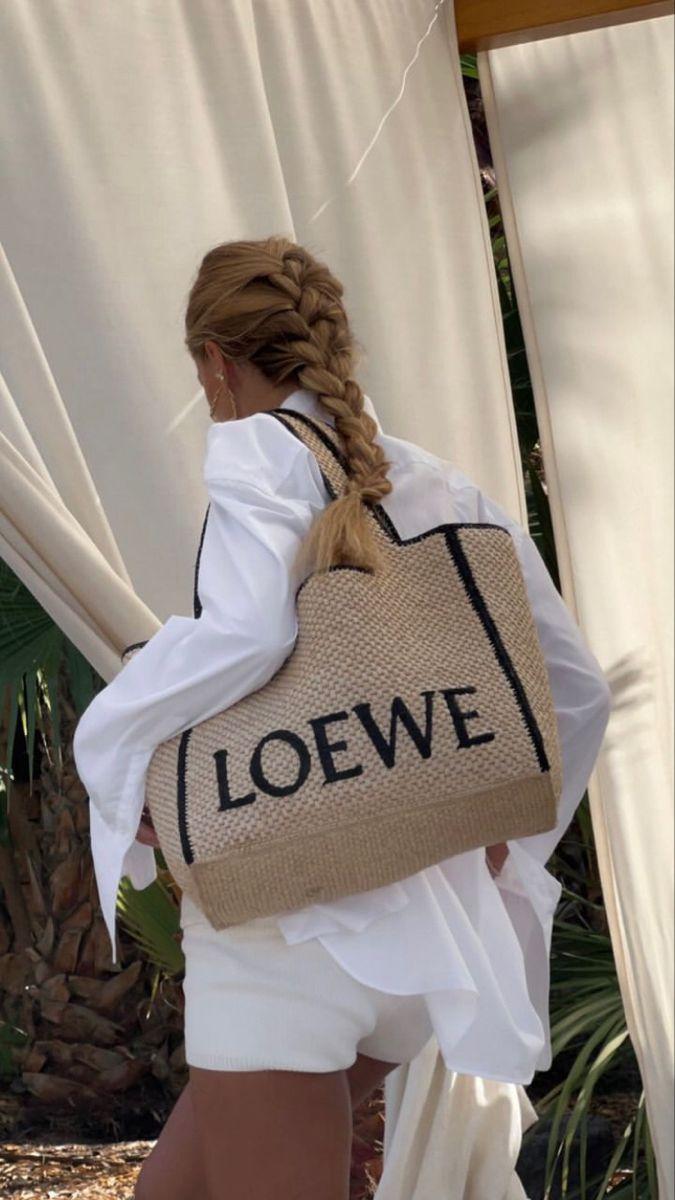 Woman with a long braid carrying a Loewe raffia tote over a white shirt