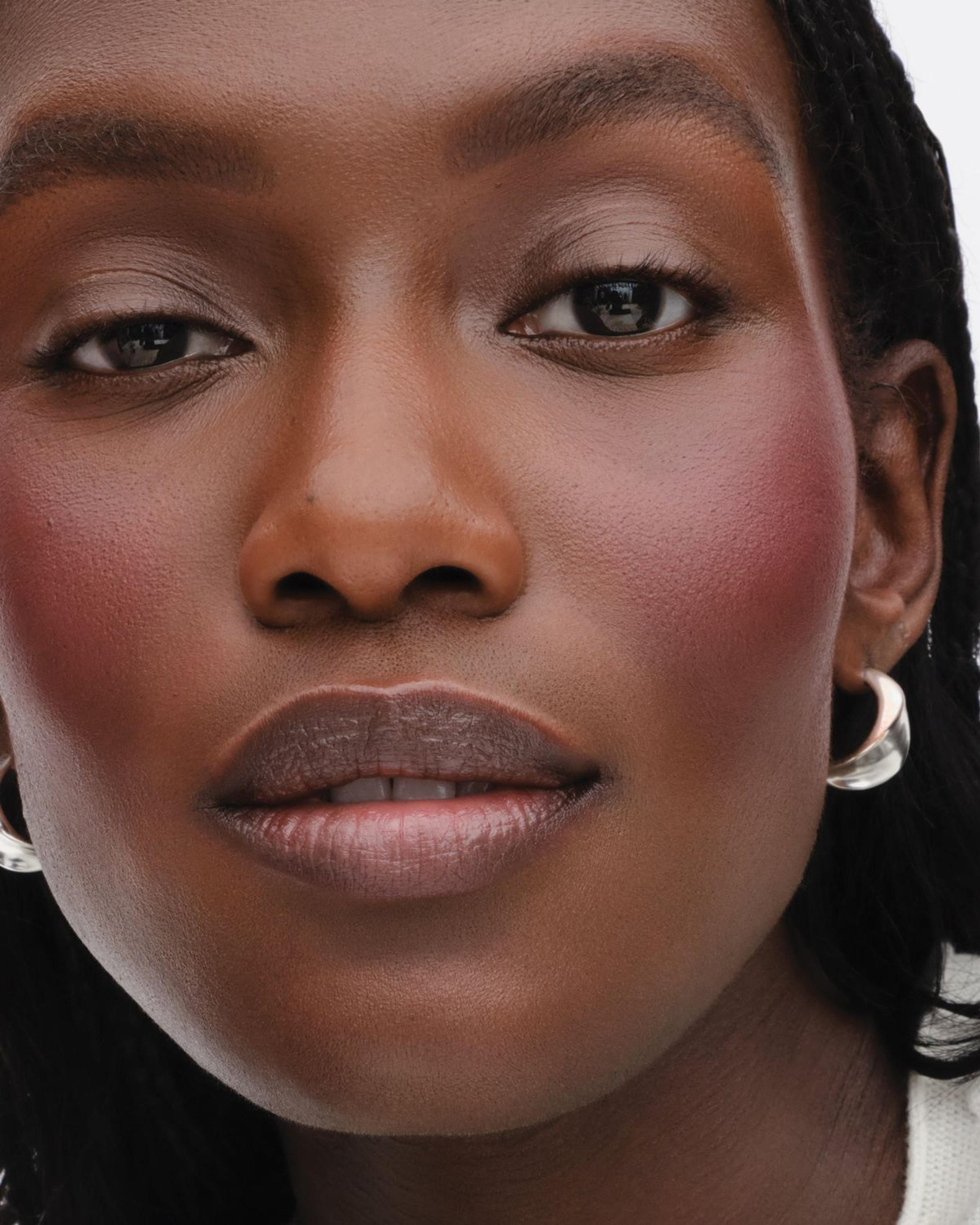 Cream blush and bronzer compacts with a fluffy brush on a pale stone surface