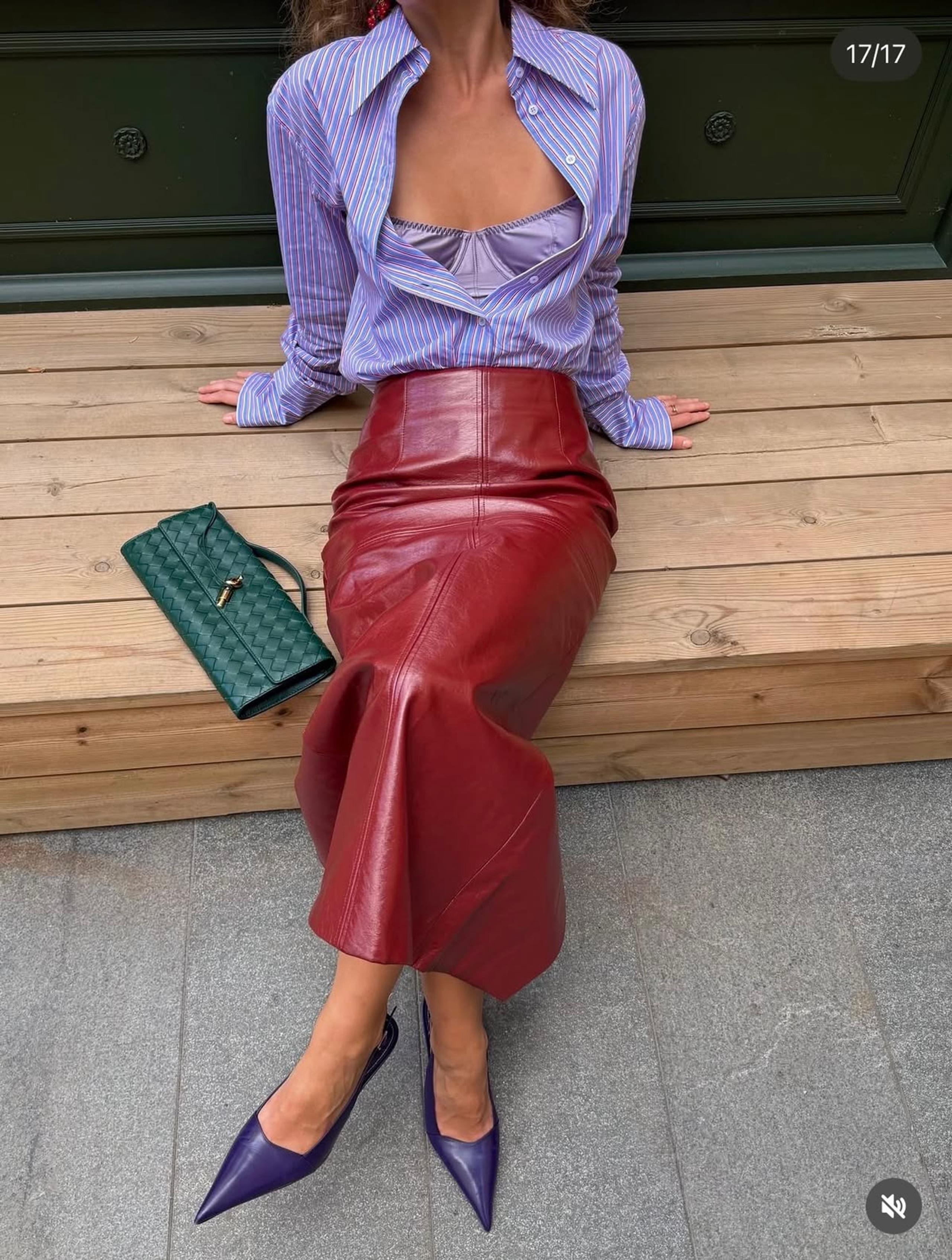 Woman in a striped shirt and red leather skirt with a green woven clutch