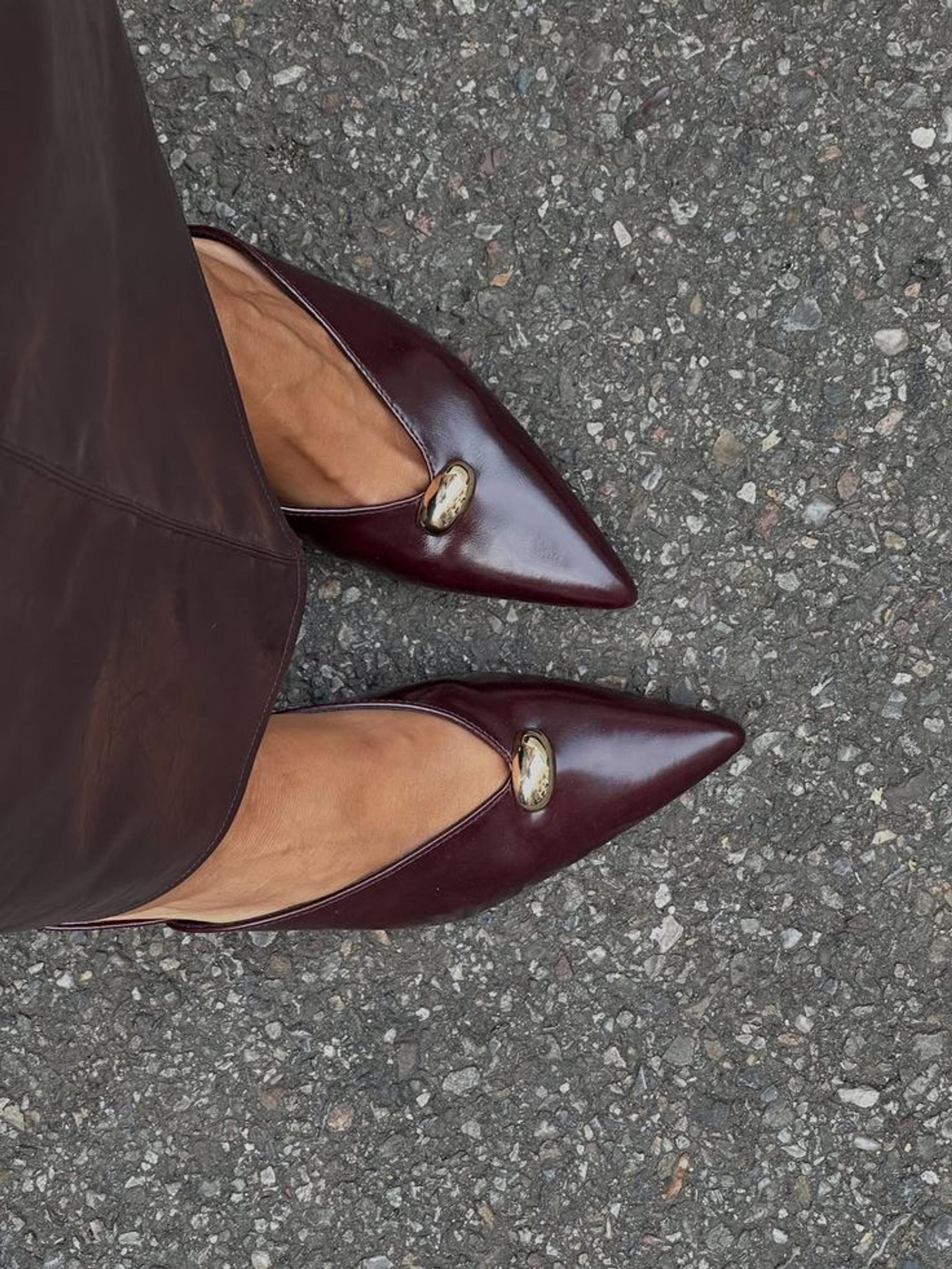 Burgundy leather pointed flats with a gold trim on grey tarmac