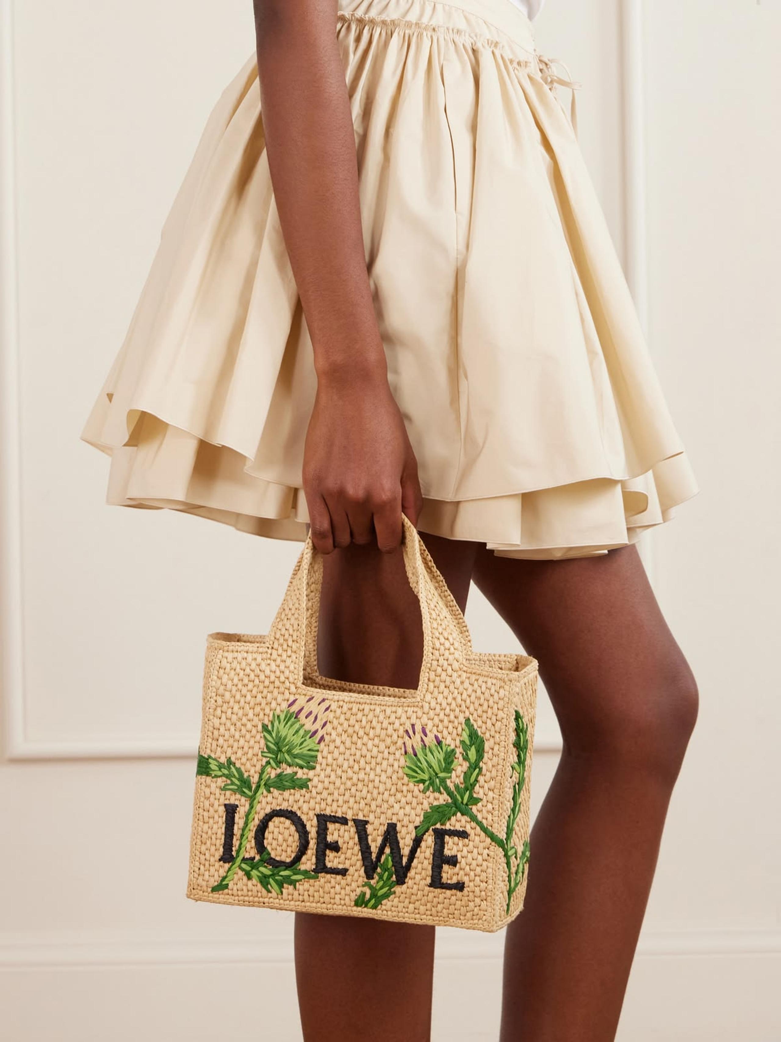 Loewe raffia tote embroidered with thistles, held against a cream ruffled skirt