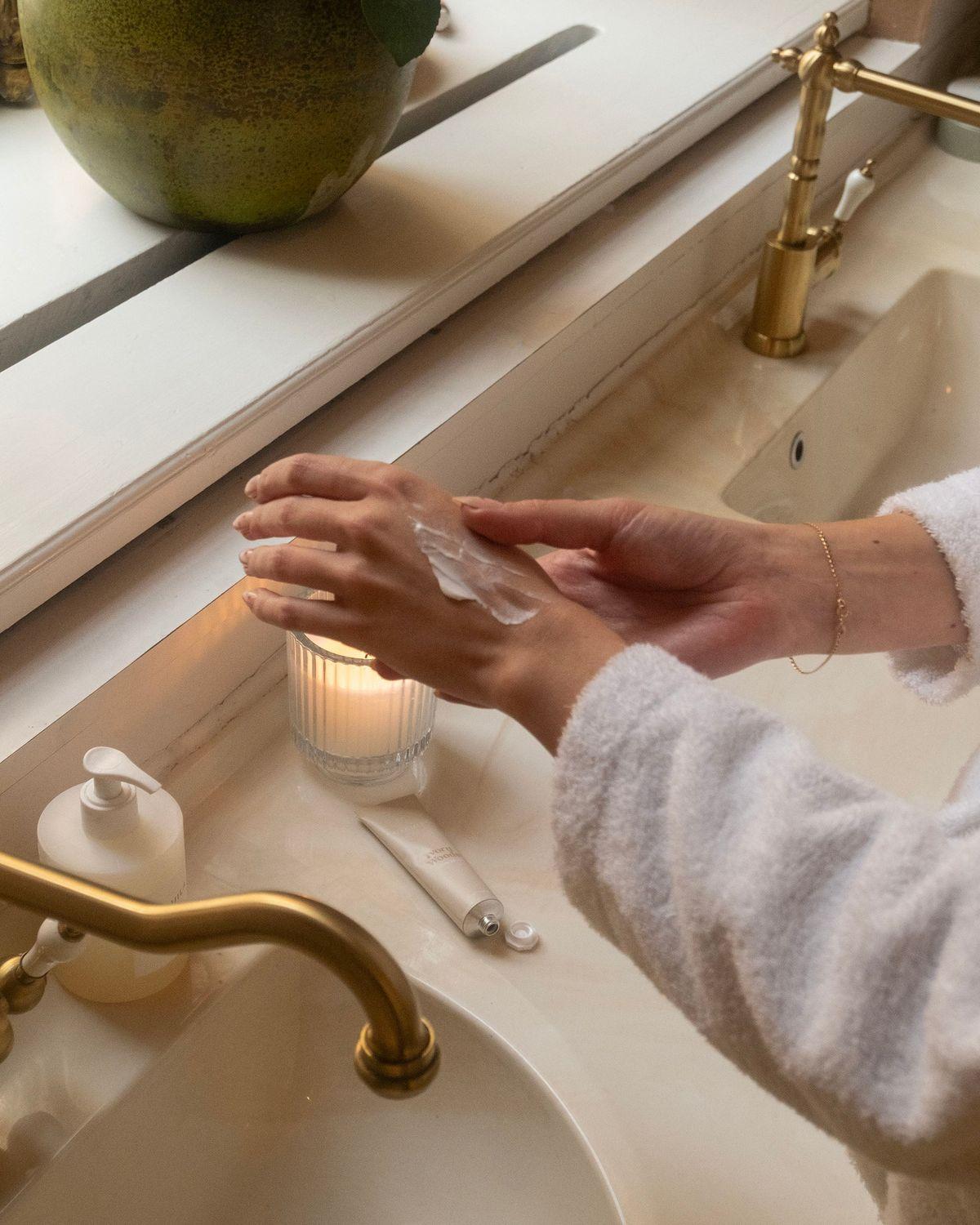 Pair of hands applying a clear serum from a glass dropper, resting on a soft cream knit