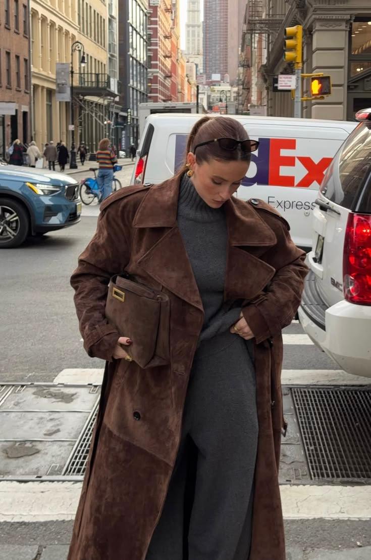 Woman in a long brown suede trench coat over a grey knit dress on a New York street