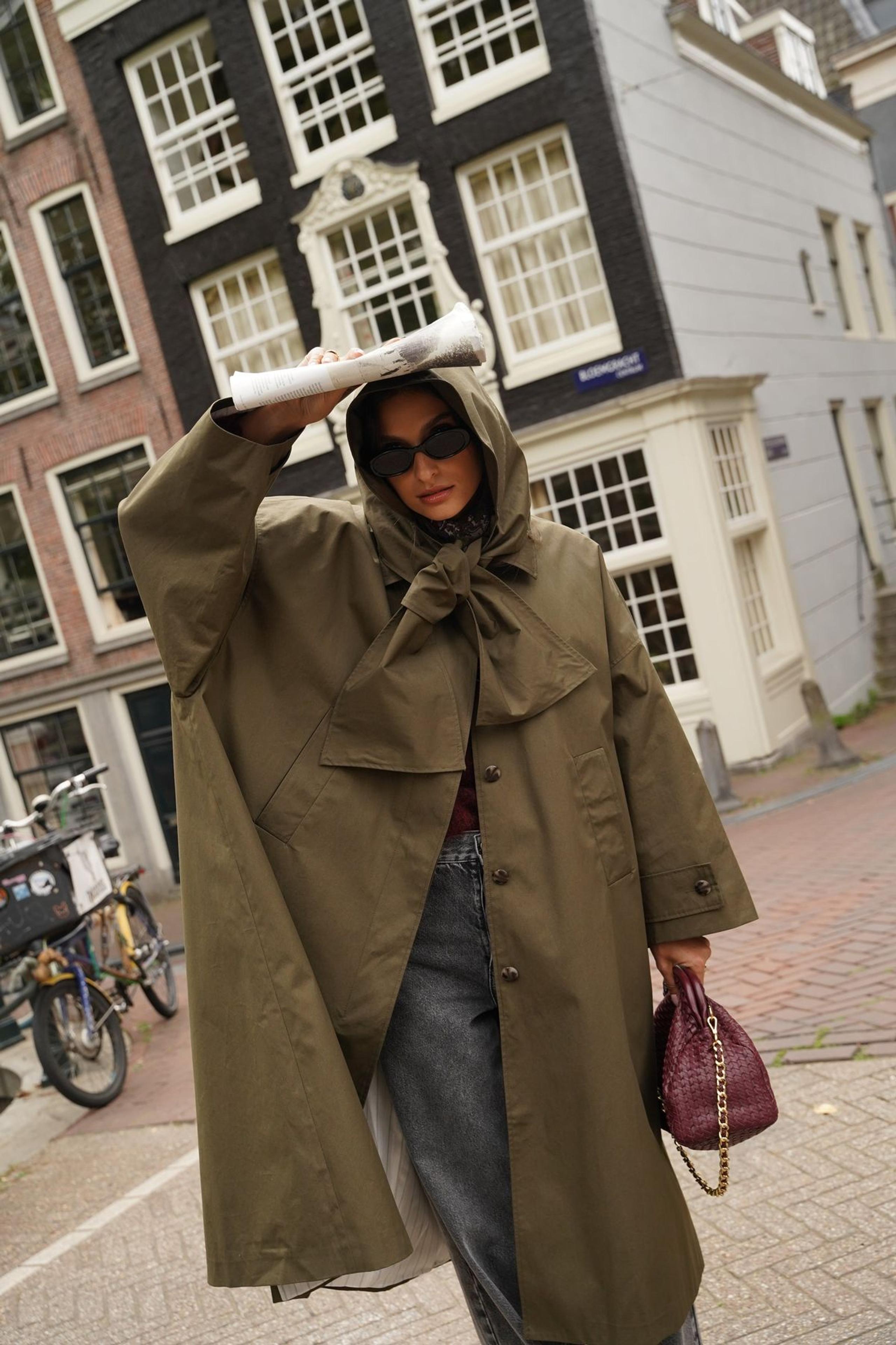 Woman in an oversized khaki hooded rain coat with a burgundy bag on an Amsterdam street