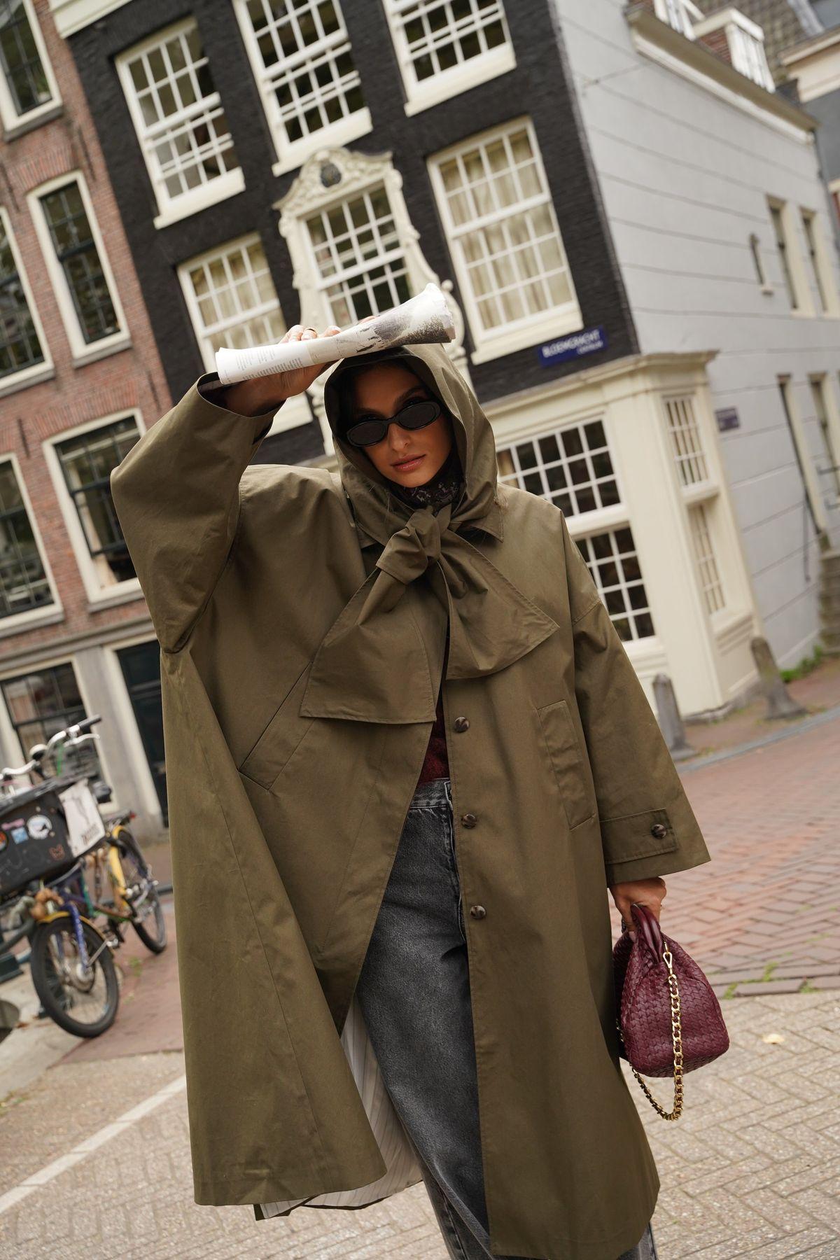 Woman in an oversized khaki hooded rain coat with a burgundy bag on an Amsterdam street
