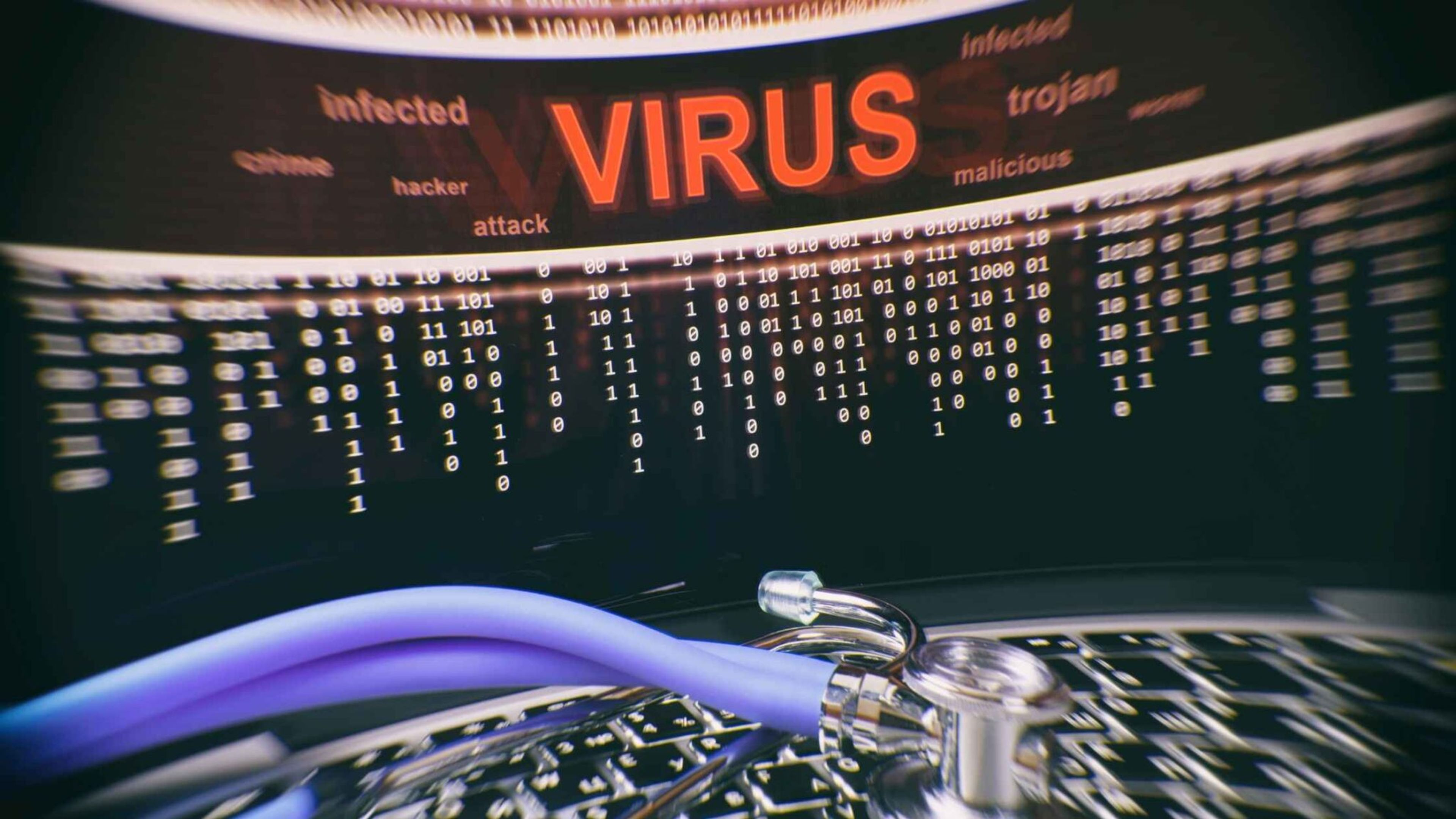 A stethoscope on a laptop keyboard, with the screen displaying "VIRUS" in red letters and binary code.
